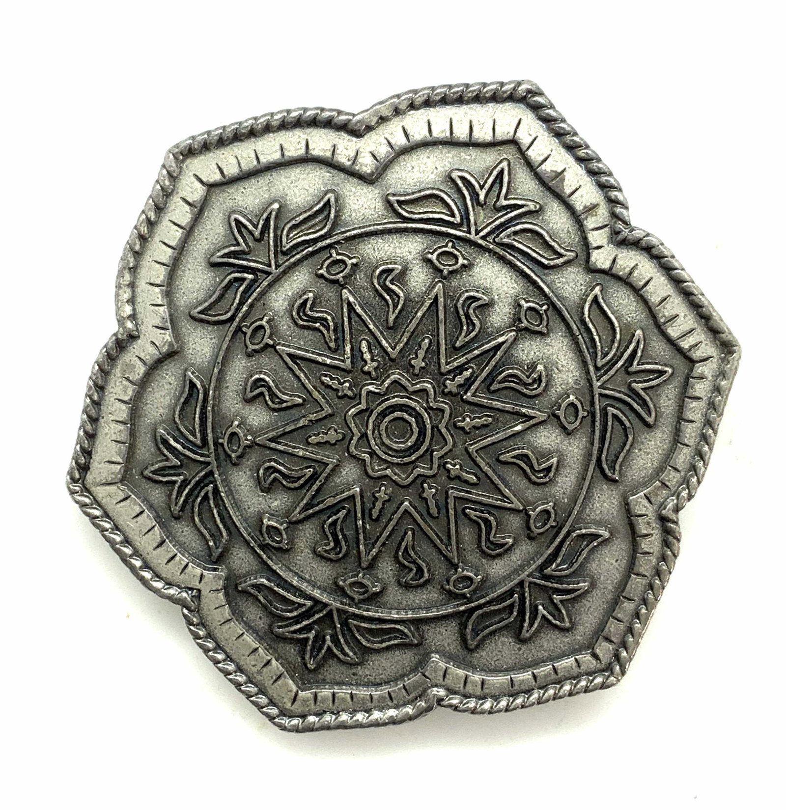 Embossed Pewter Belt Buckle Wearable Accessory: Weighted buckle, possibly pewter, floral design in relief, center star/ sunburst medallion. Etched border detail with roped rim. Just under 3 in diameter. Backside has moveable swivel and prong catch.