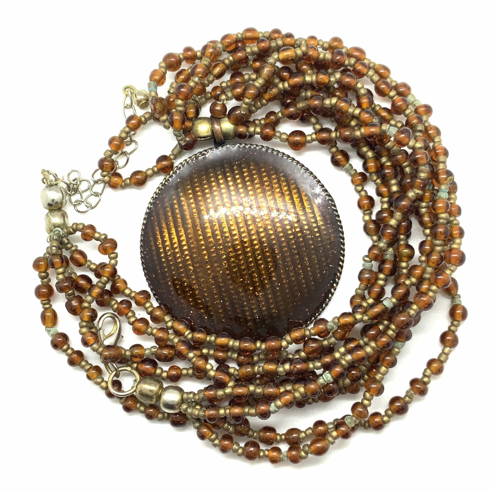 Five Strand Beaded Pendant Necklace, Jewelry: Five strand necklace with deep amber toned transparent beads. Large circular shimmer pendant in the center. Pendant is also a deep amber tone. Pendant is attached to necklace with a bail. Lobster clas