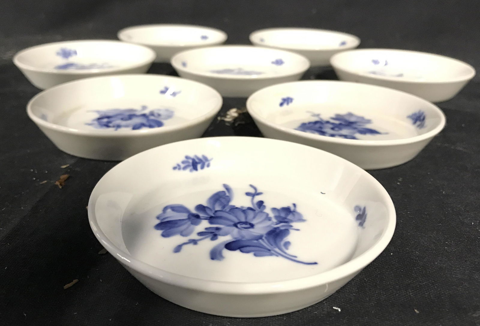 Set 8 ROYAL COPPENHAGEN Porcelain Coasters: Undersides of each piece read ROYAL COPPENHAGEN DENMARK. Lot includes 8 coasters, each are porcelain. Coasters are white with blue toned floral and leaf detail. Each measures approximately 3.5 inches
