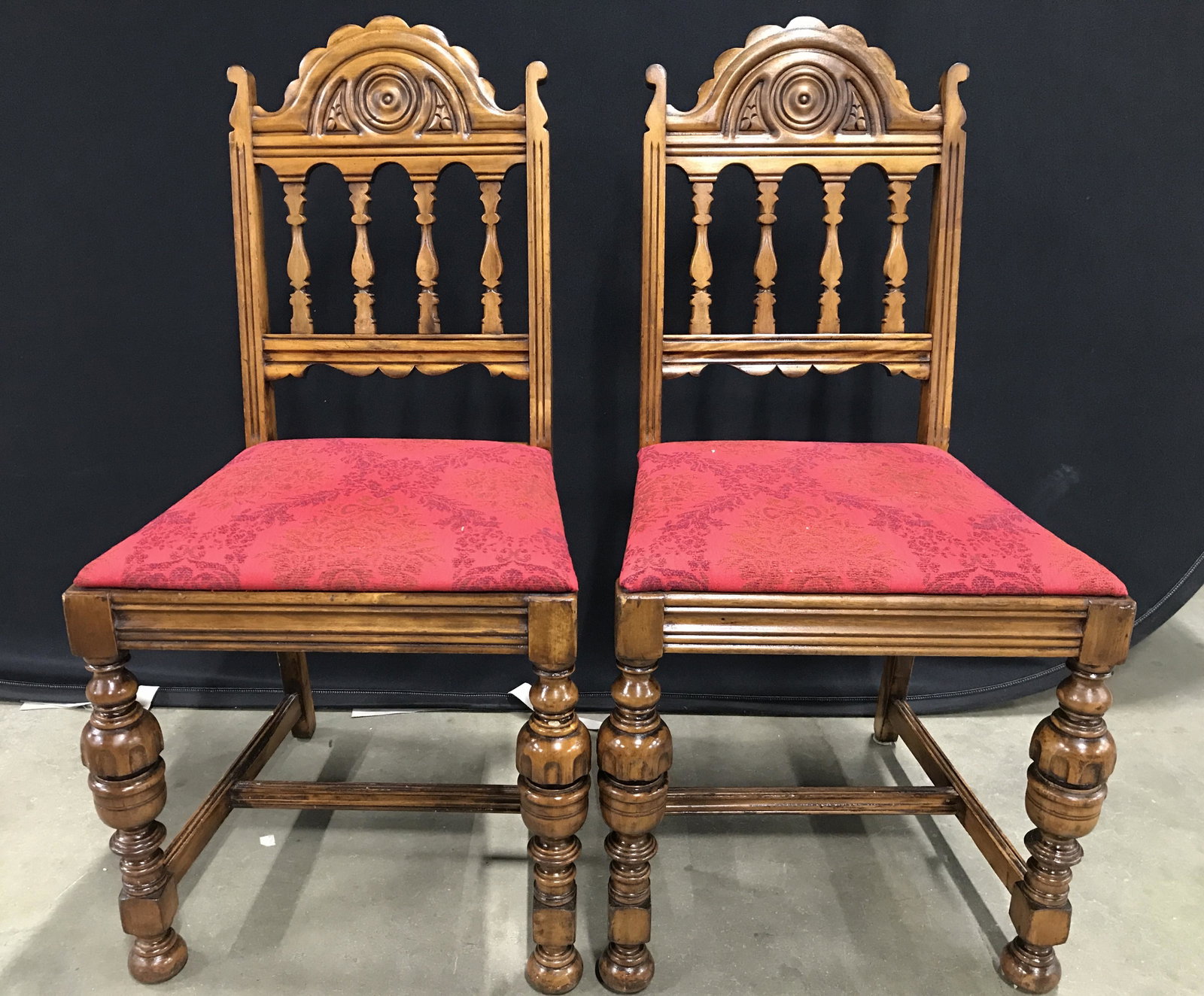 Vintage Intricately Carved Wooden Side Chairs: Side chairs are wooden. Each has intricately carved detail. Chairs are vintage possibly antique. Chair legs have stretchers in between. Seat cushions are upholstered with red floral and leaf detailed 