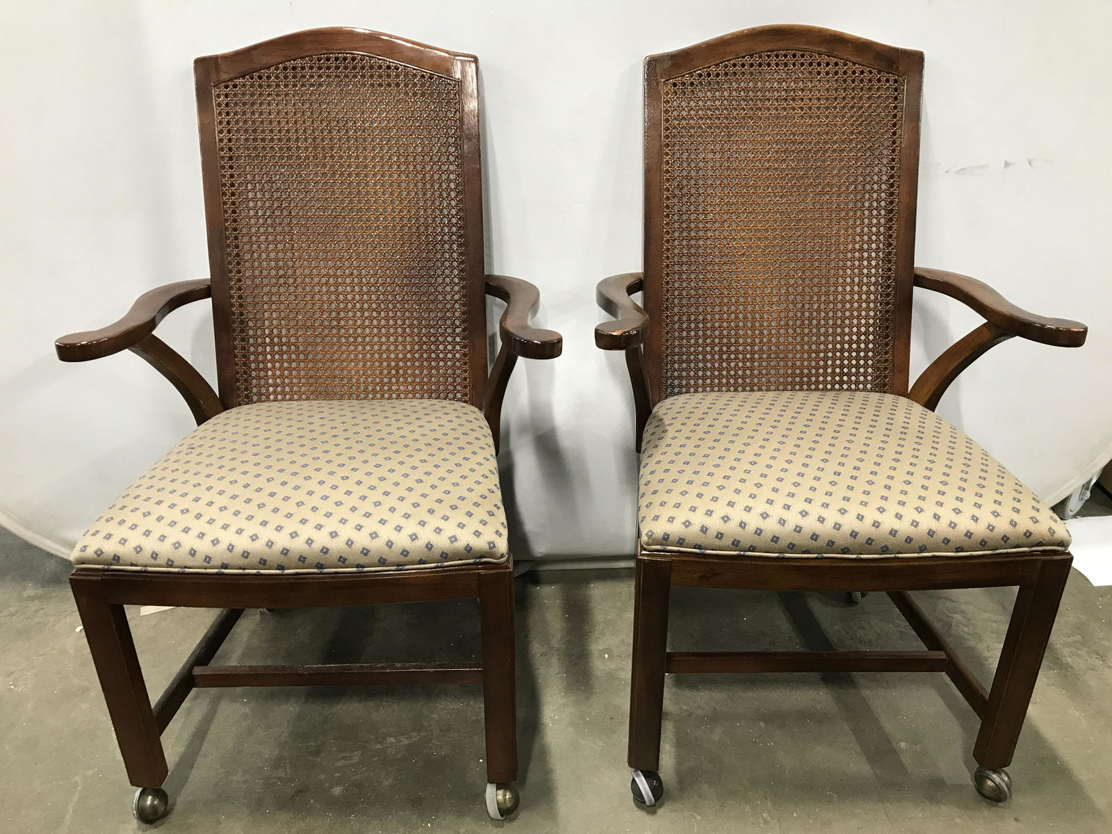 Pair DREXEL HERITAGE DINING CHAIRS W Casters: Undersides of each chair has tag which reads DREXEL HERITAGE. Each piece is wooden with caned backrest. Chairs have carved wooden armrests. Each seat has multi toned geometrically detailed upholstery.