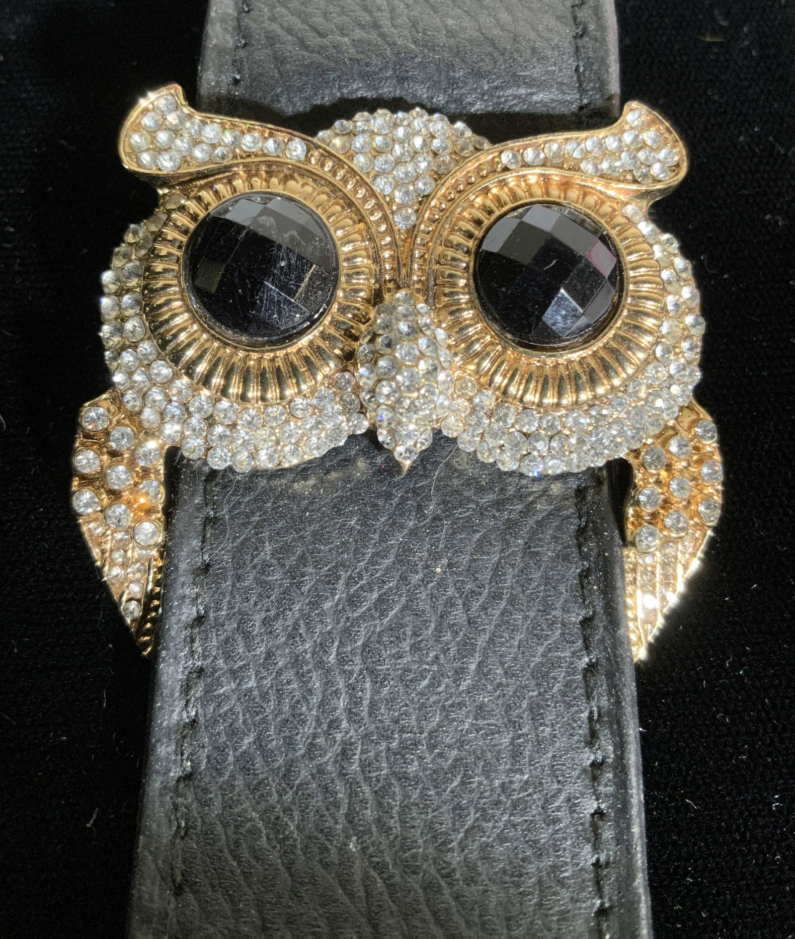 Crystal Owl Leather Wristband, Jewelry: Black leather wristband, 1.25 in. W, slidable accessory of Large owl eyes with costume jet bead eyes, halo gold tone metal in relief, eyebrows, feathers. Piece slides on leather band. Adjustable with 