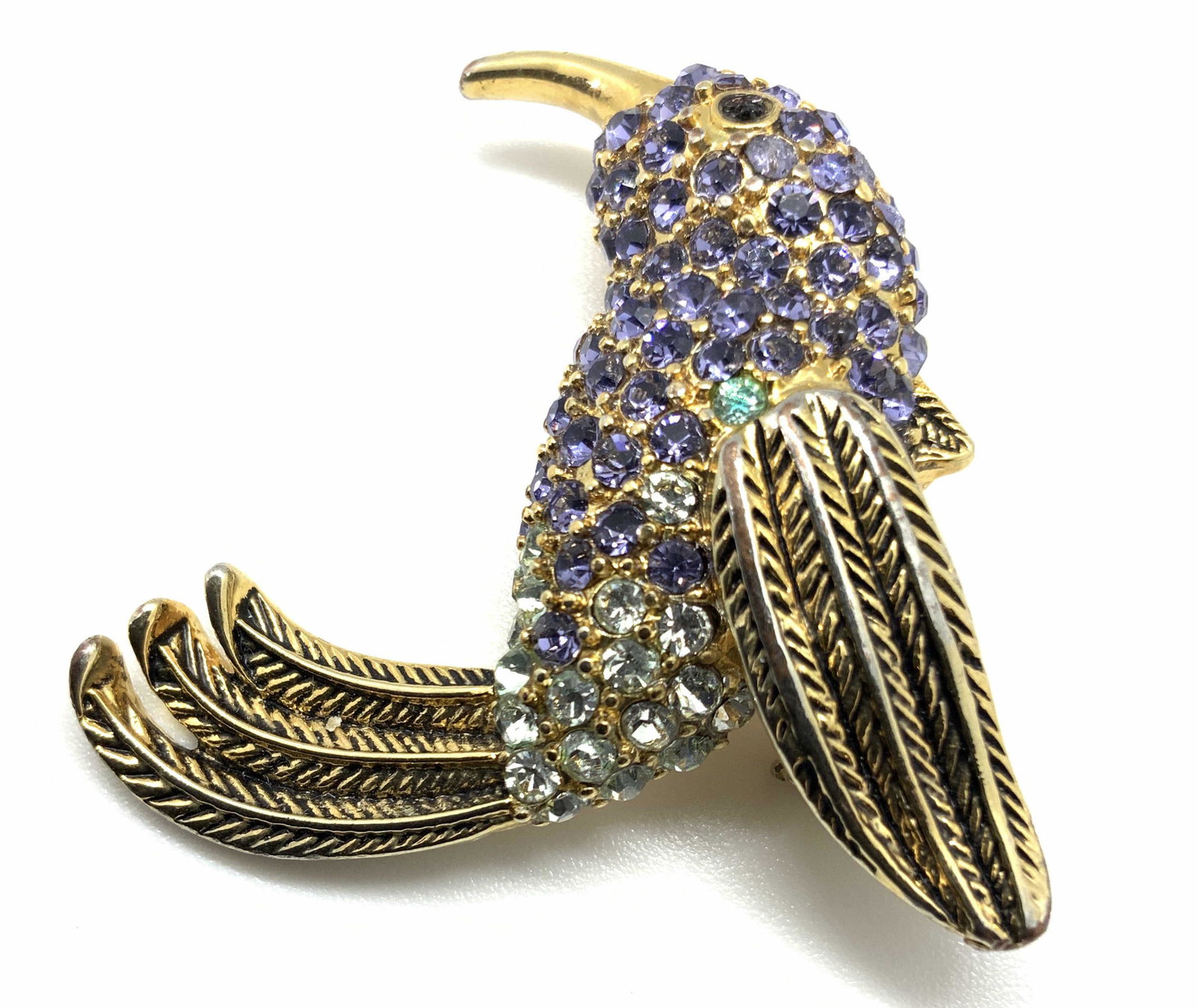 Vintage Signed MONET Crystal Hummingbird Brooch: A vibrant crystal hummingbird brooch. The hummingbird has a polished & etched gold tone metal body with bezel set crystals throughout. The crystals coloring includes greens, light purples, and clear f