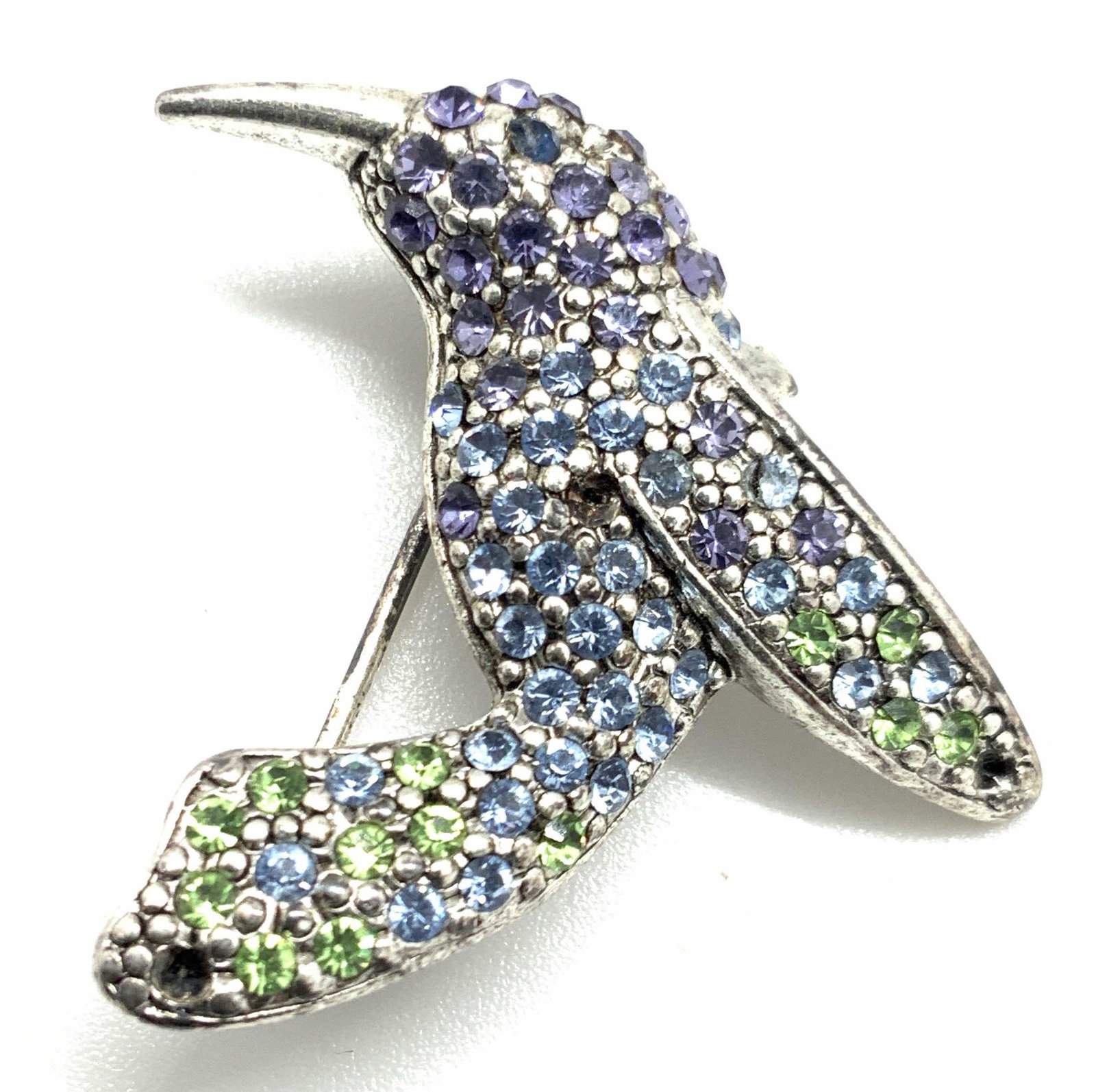 MONET Vintage Signed Crystal Hummingbird Brooch: A vibrant vintage crystal hummingbird brooch. The hummingbird has a metal tone metal body with bezel set crystals throughout. The crystals coloring includes greens, light purples, and clear faceted cr