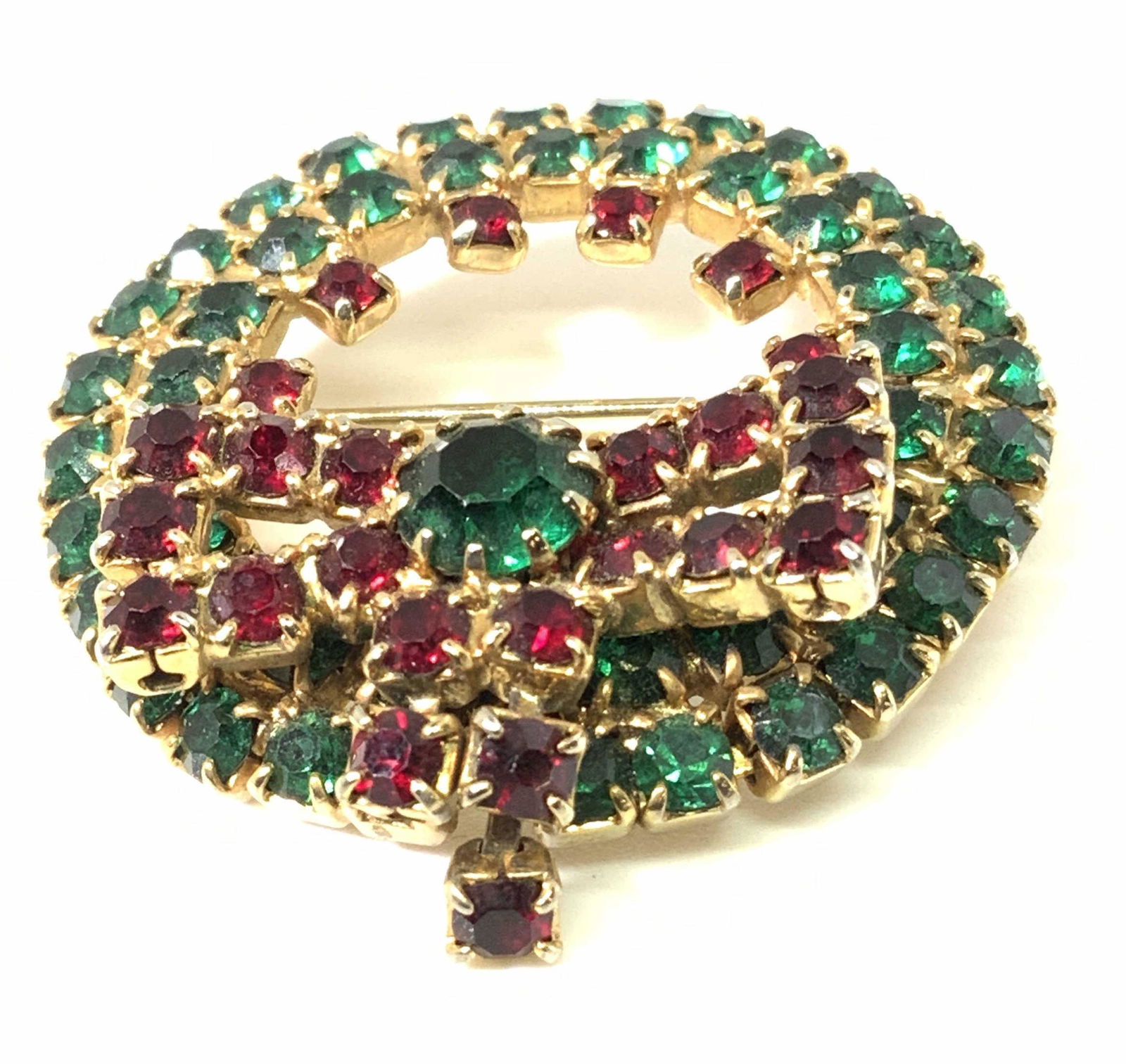 Vintg Articulated Rhinestone Holiday Wreath Brooch: A vintage faceted rhinestone brooch in the form of a holiday wreath. The wreath is adorned with red and green prong set rhinestones. The wreath has a red ribbon offset towards the bottom center with o