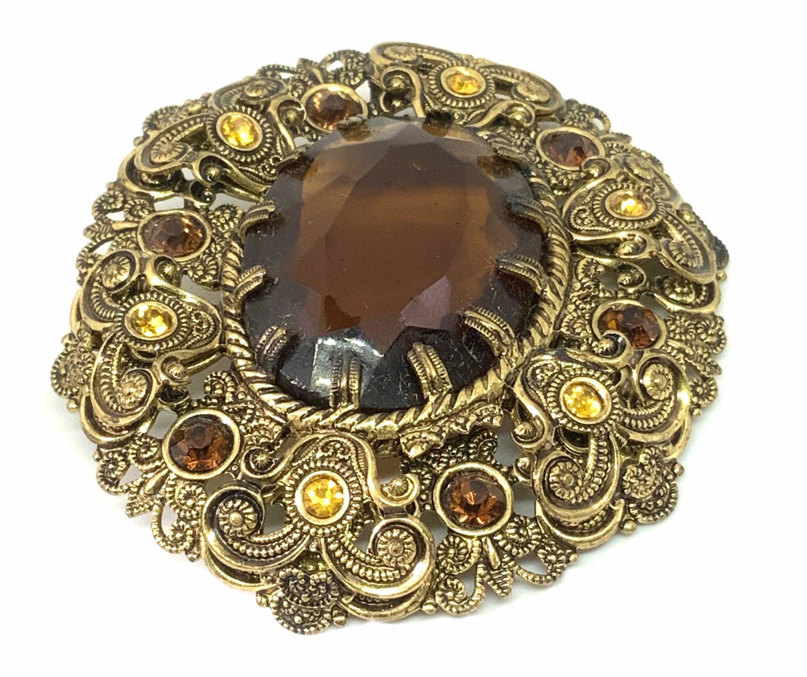 Vntg Victorian Style Crystal Filigree German Pin: A vintage antiqued gold tone metal filigree pin / brooch with a rich brown crystal set in the center. The pierced metal filigree is intricate and studded with bezel set, faceted yellow & amber toned c
