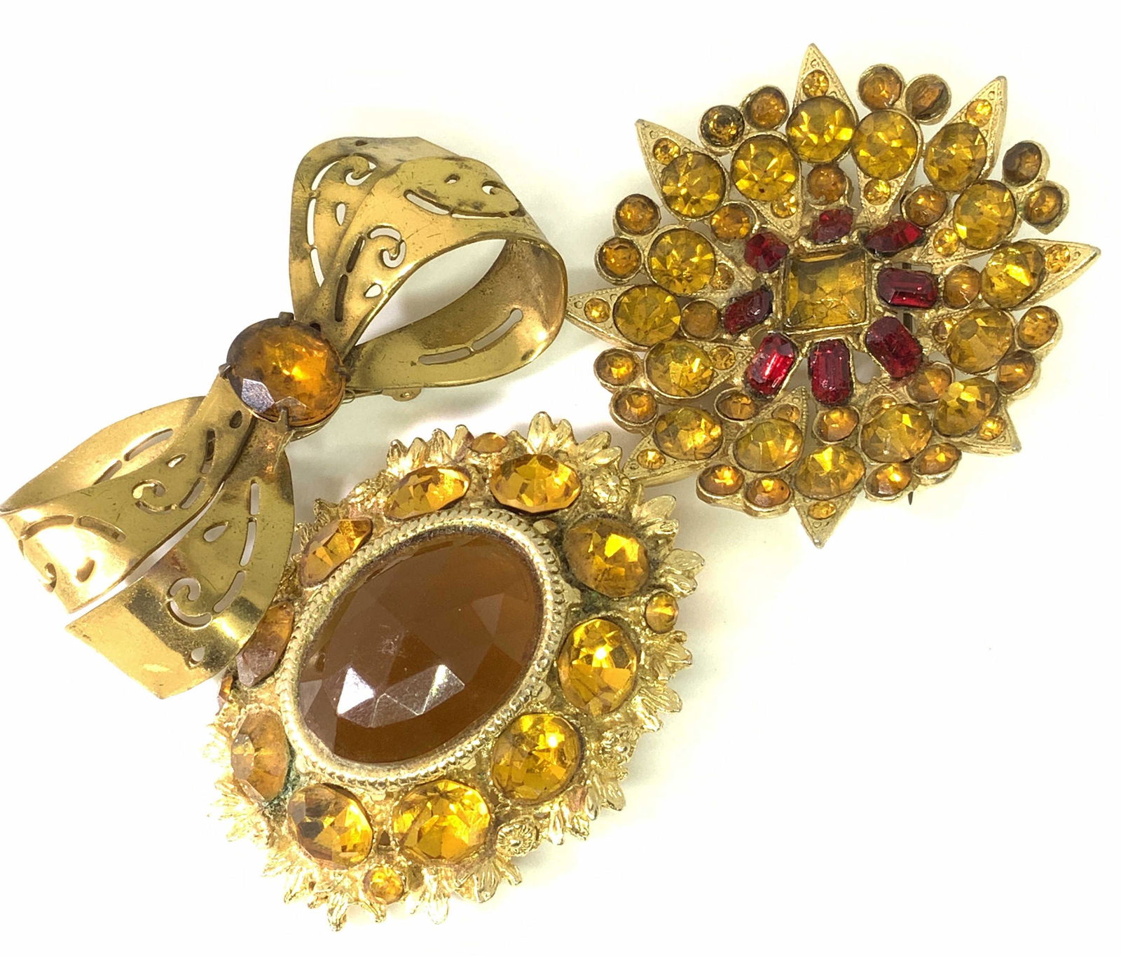 Lot3 Vntg Amber Toned Fashion Brooches, Coro more: Three vintage brooches decorated with amber and yellow hued faceted rhinestones. One brooch possess red faceted rhinestones. Each brooch possesses a unique form. A Victorian style brooch, a ribbon bro