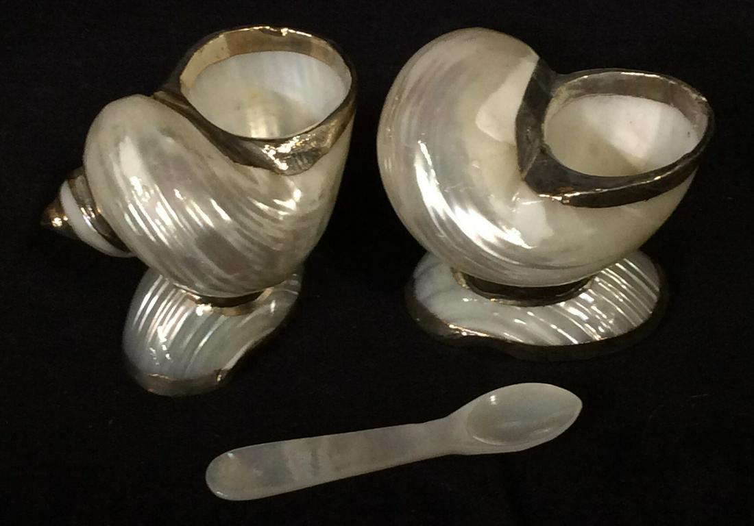Luxury Pair Mother Of Pearl Salt Cellars w Spoons: Total 3 items. Mother of Pearl snail shell Salt cellar with coating of silver toned metal rims, possibly sterling silver. 1 spoon included, 2.25 in. Long. Shell containers measure 2 x 1.5 in. Ht 2 in.