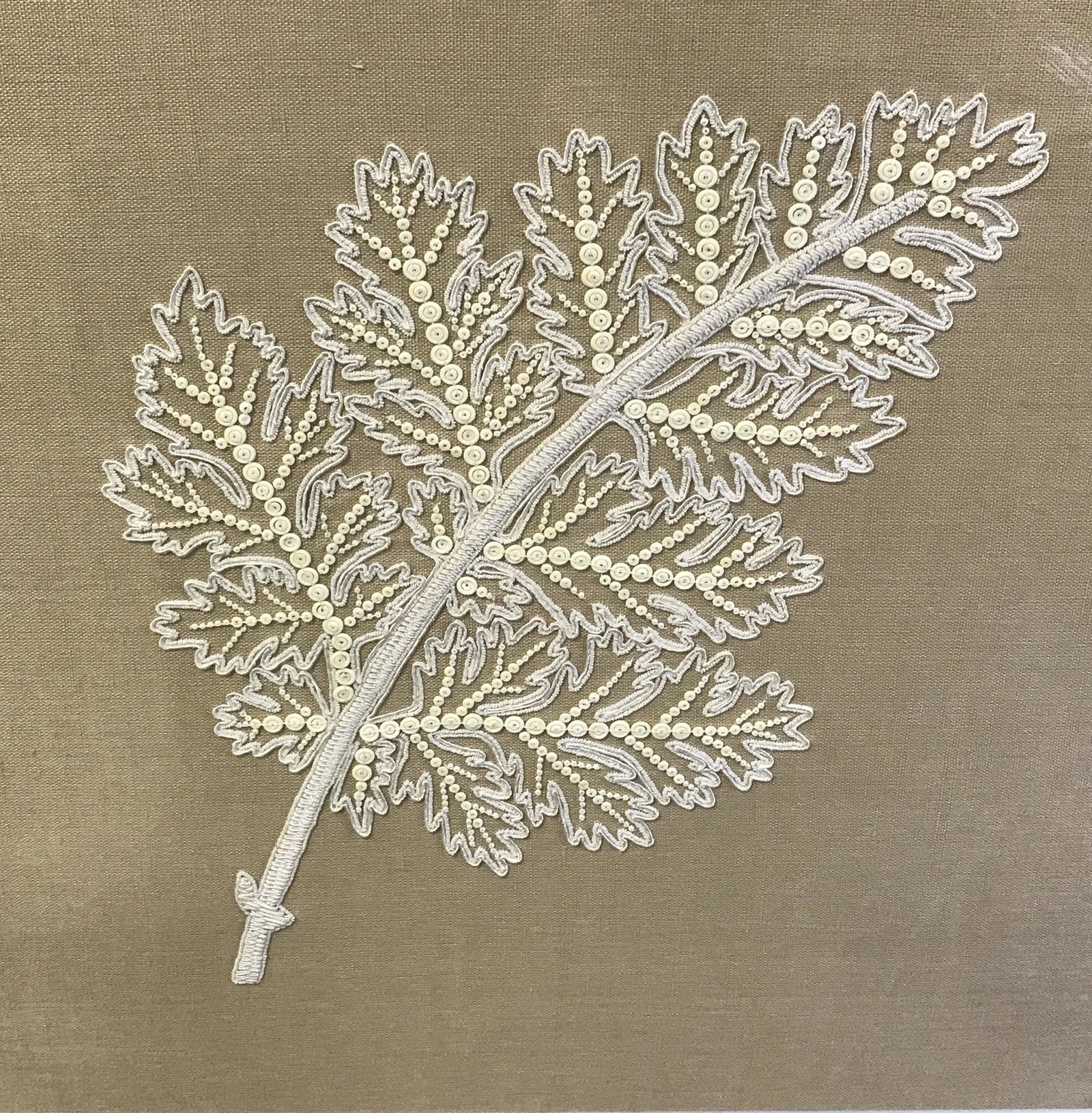 Mounted Embroidered Linen in Shadowbox: Mounted Embroidered Linen in shadowbox, label to reverse reads ‘Trowbridge’, subject a board of tan linen with white embroidery and beads in the shape of a leaf mounted on a board, white matting, 