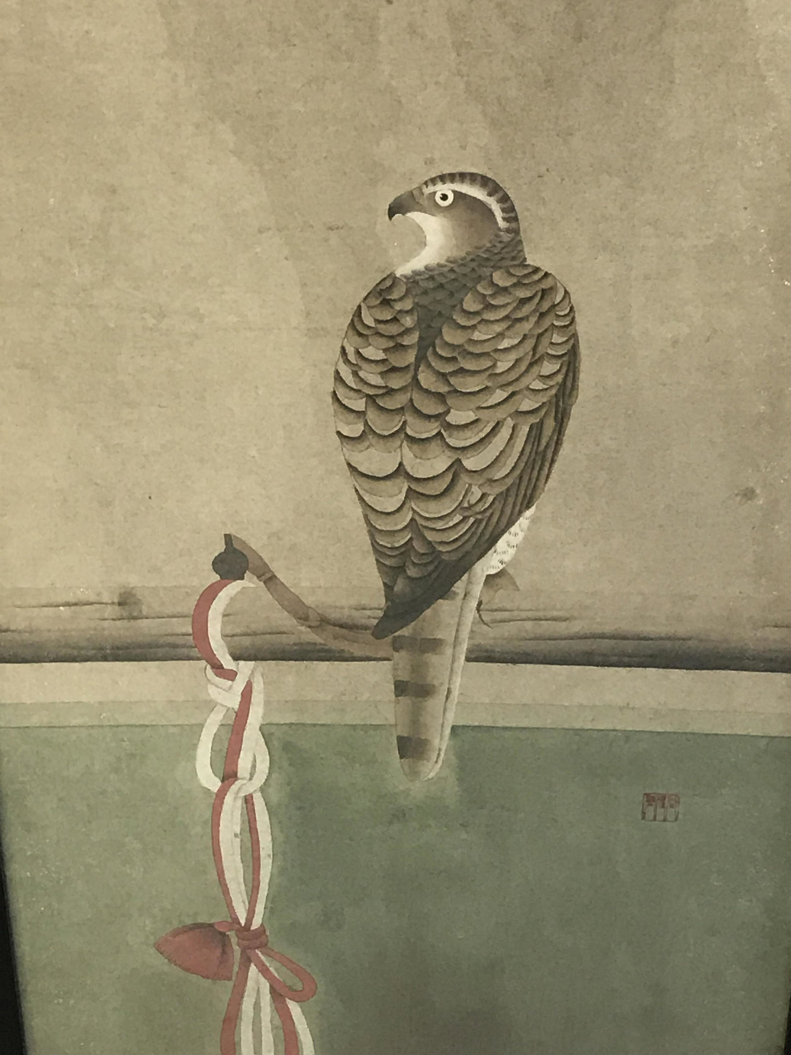Signed Chinese Hand Painted Bird Artwork: Chinese Hand Painted Bird, red Chinese character stamp to lower right section, subject a bird of prey tied to a pole with ropes twisted round it, matte black wooden frame, measures 36.5 inches tall an