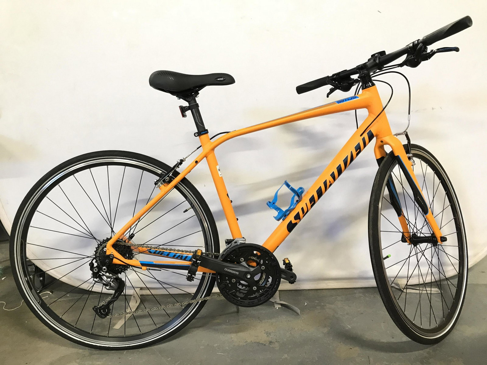 SPECIALIZED SIRRUS ELITE Bicycle: Bicycle is marked SPECIALIZED SIRRUS ELITE. Piece has tones of Orange, blue & black. Bike has SHIMANO Pedals & ALPINE seat. Piece measures approximately 64 inches long 24 inches wide at handle bars 38