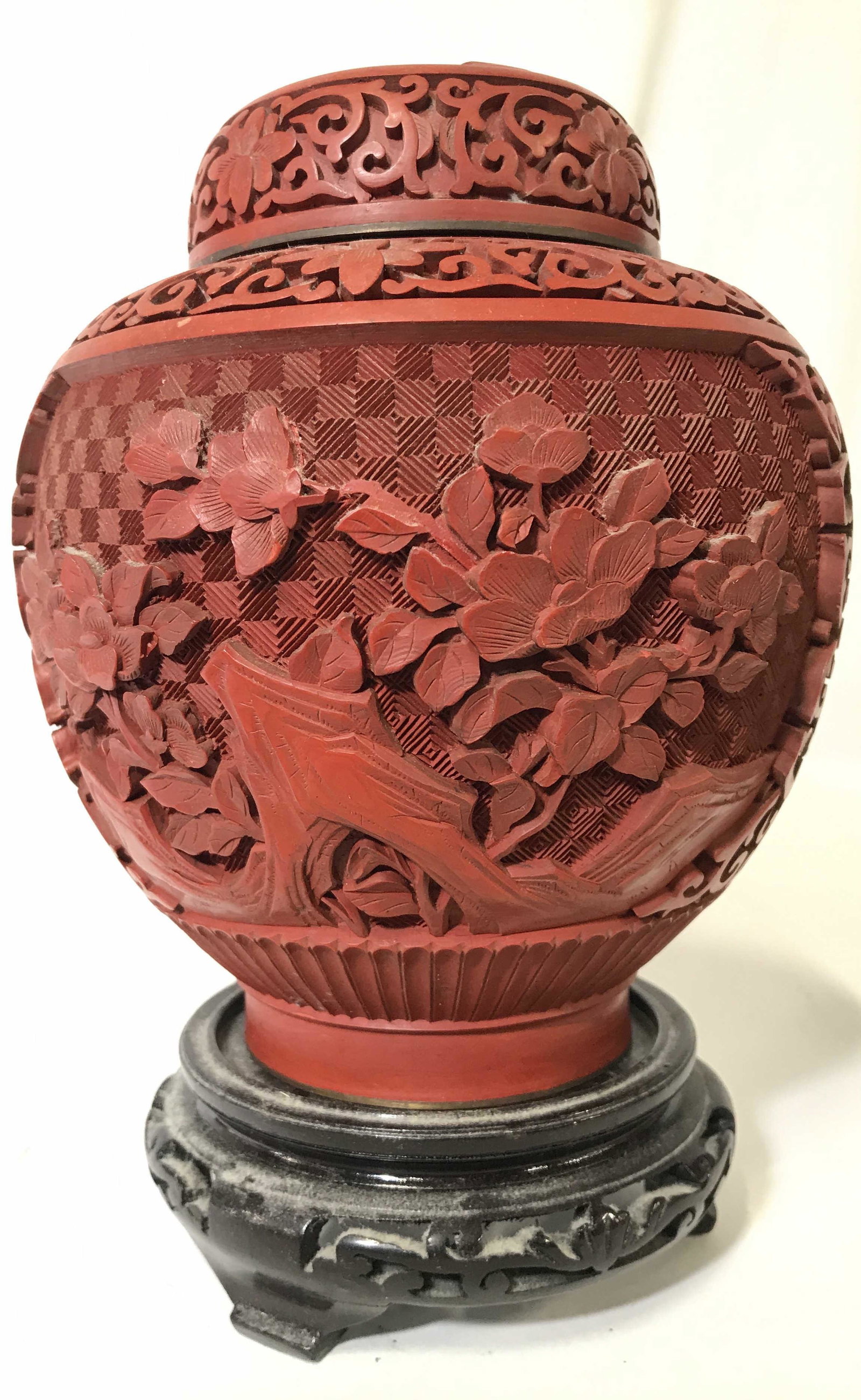 Vintage Asian Cinnabar Ginger Jar W Stand: Ginger jar is red toned and vintage. Piece has intricately carved floral vine & leaf detail. Piece includes carved wooden stand. Jar measures approximately 7 inches tall 6 inches wide. Cinnabar vase, 