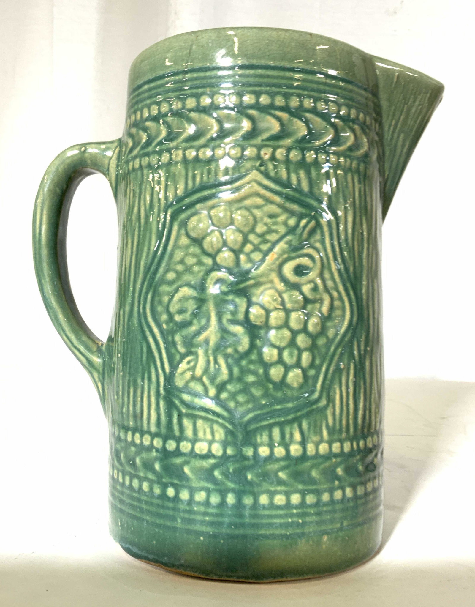 Vintage Antique Green Glazed Ceramic Pitcher: Collectible vintage pottery, ceramics, with shiny glazing, medallions of grapes and leaves in relief, geometric border designs and stripe striping sides, vessel, pitcher, vase, tableware, decorative o