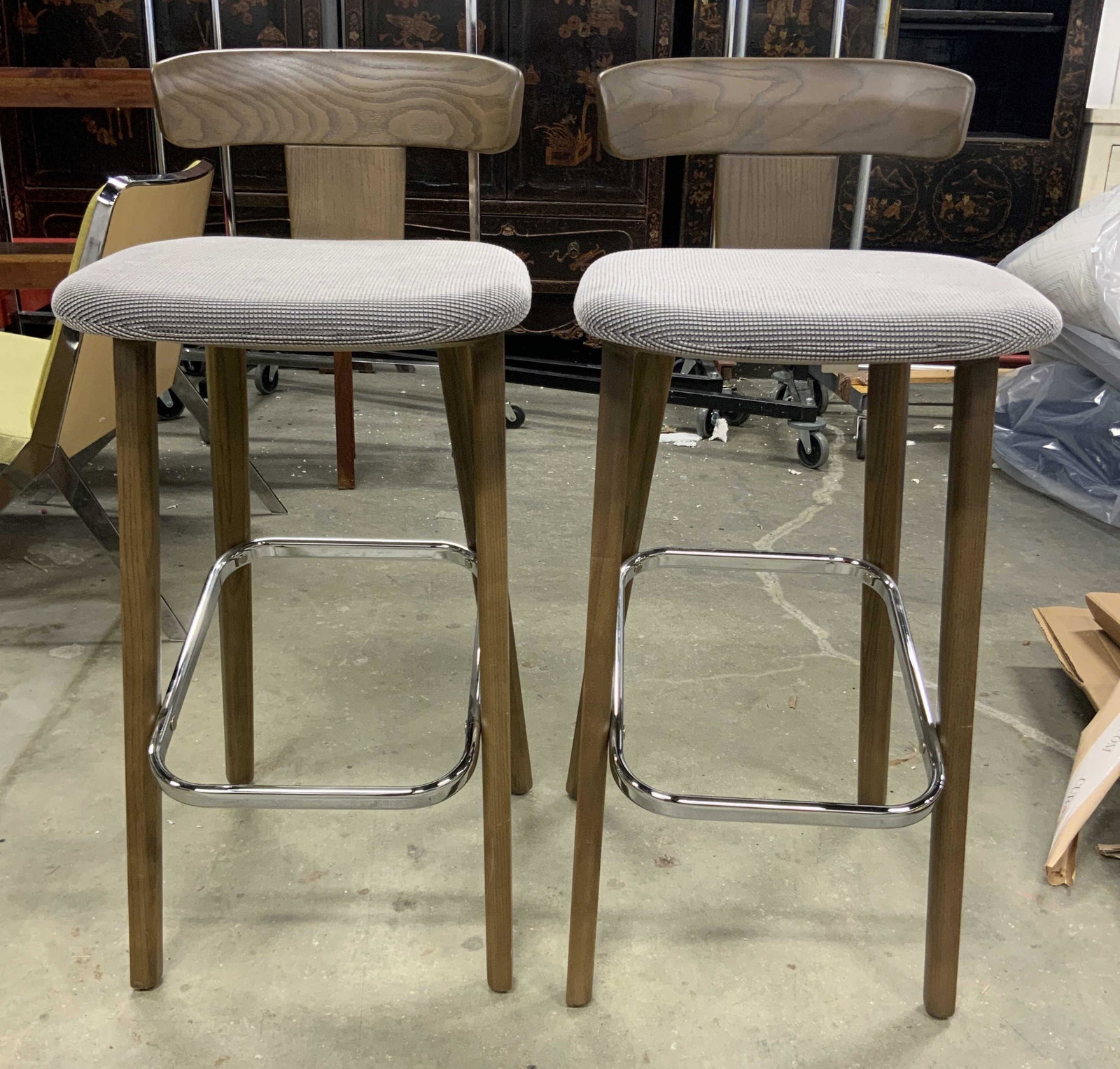 Pair Mid Century Modern Bar Stools W Backrests: Lot includes 2 bar stools. Each are mid Century Modern. Frame Of stools appear to be wooden. Each have slate toned seat cushions. Stools have chrome stretchers between legs. Each measures approx 38 in