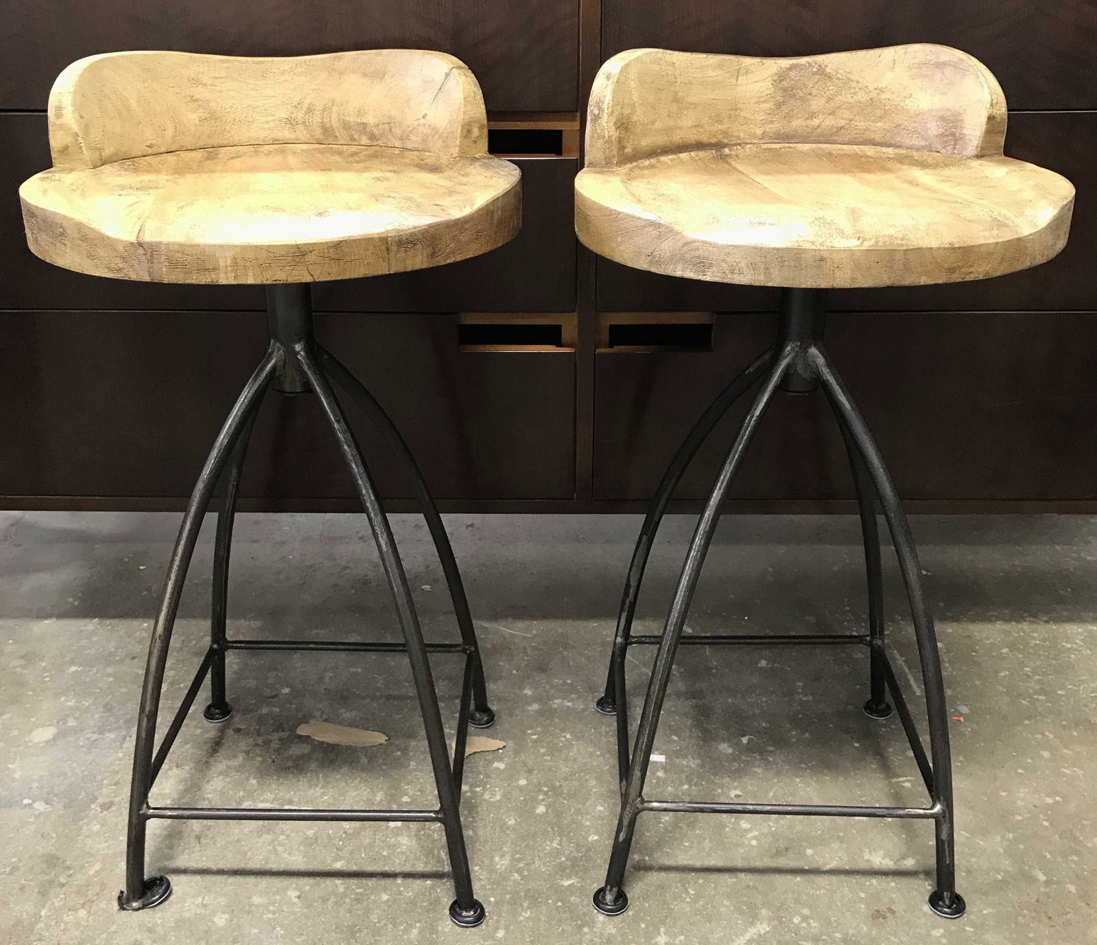 Pair Wood Seat Metal Base Bar Stools: Bar stool seats are wooden. Each seat is tan toned. Bases of stools are metal, possibly iron. Bases have 4 legs with stretchers in between. Seat area swivels. Each appear to possibly be vintage. Each 