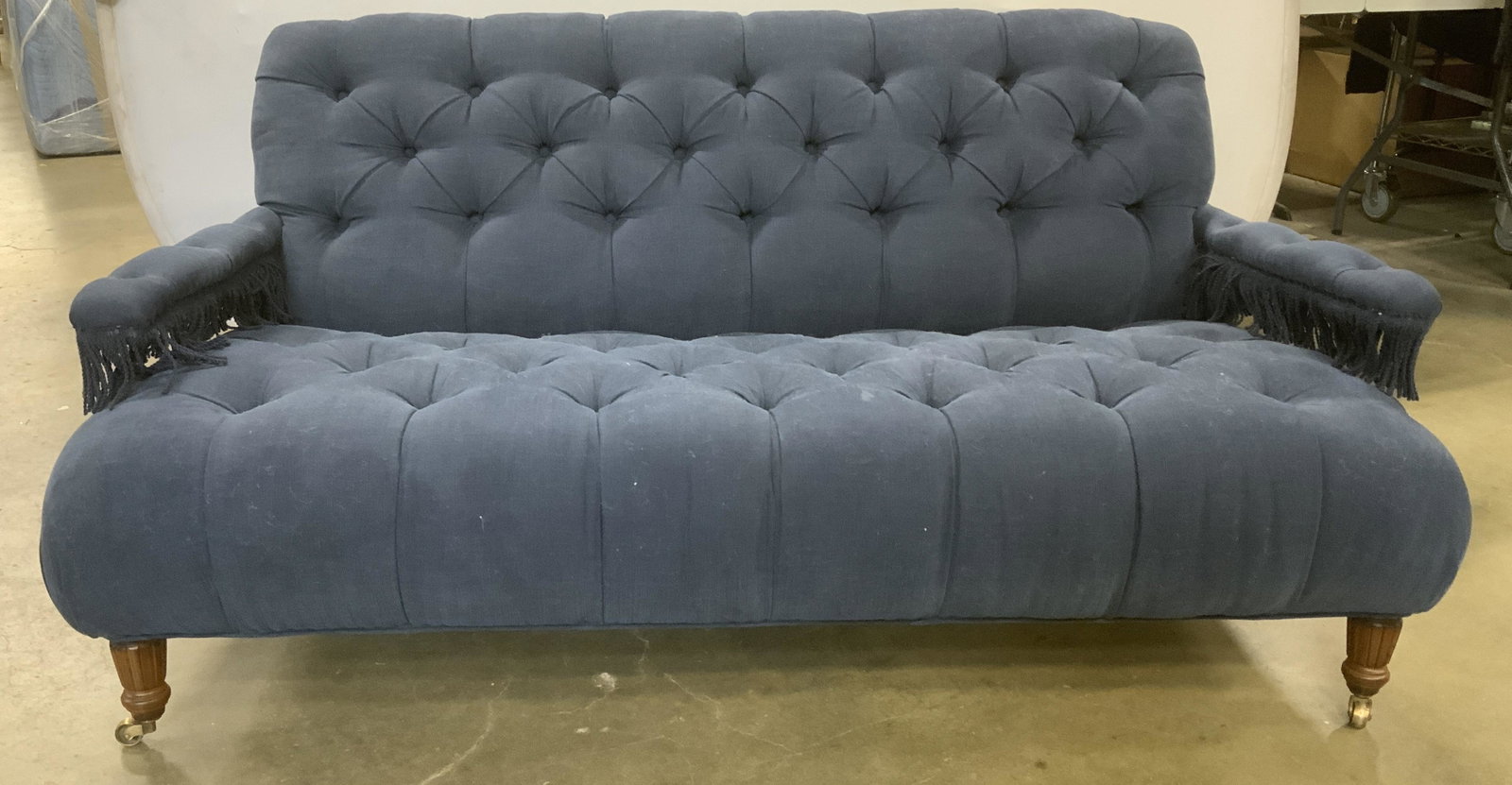 JOHN DERIAN COMPANY Coop Sofa: Tufted, chesterfield style, coop sofa. Designed and manufactured by JOHN DERIAN COMPANY. Front legs rest on castors, sofa arms decorated by braided fringes. Upholstery is colored in midnight blue tone