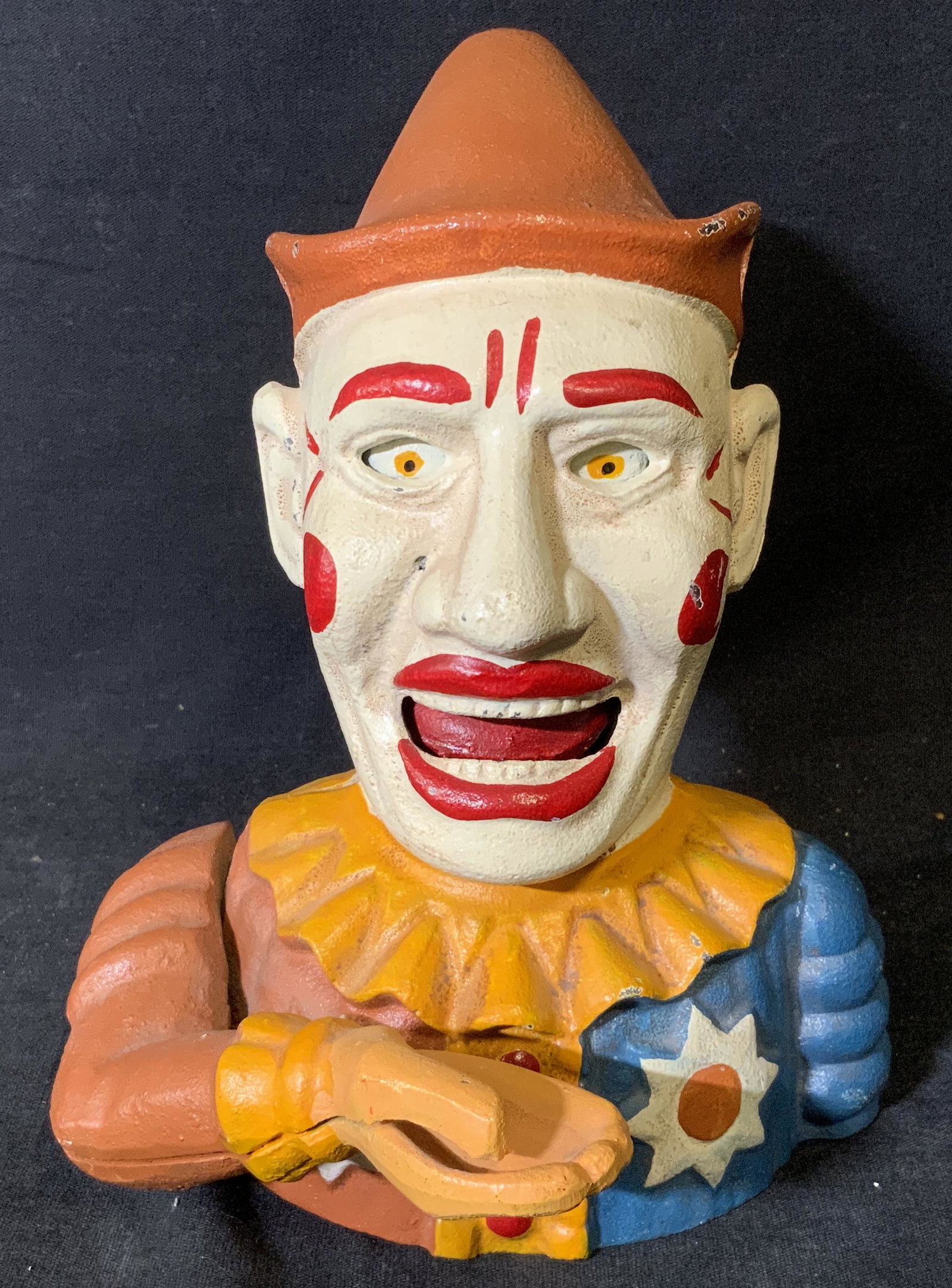 CLASSIC IRON Cast Iron Painted Clown Piggy Bank: Cast iron hand painted clown piggy bank, inscription to underside reads ‘Classic Iron’, subject a clown in yellow and blue with hand extended, coin to be placed in hand of clown, once lever is swi