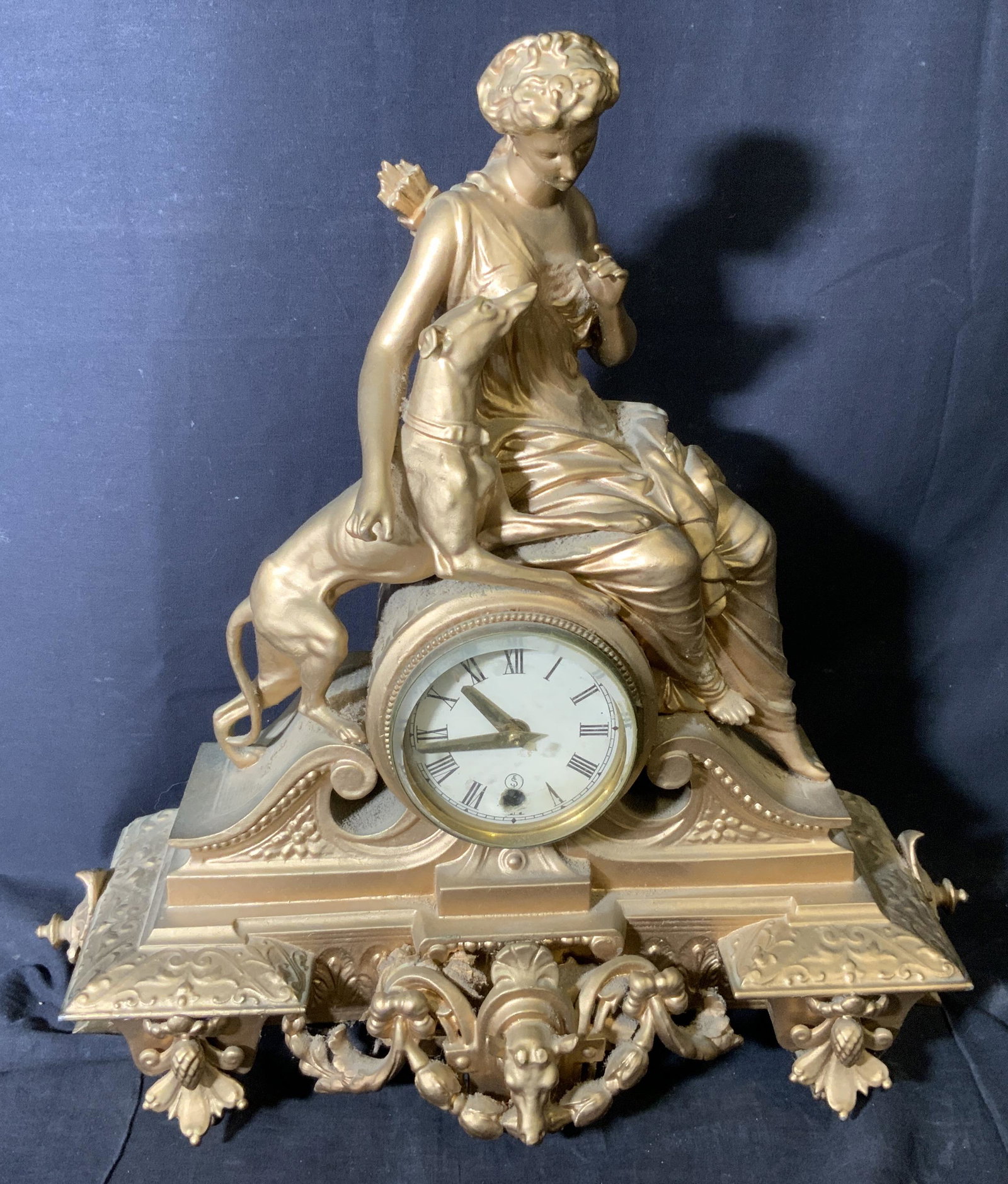 White Metal Rococo Sculptural Mantel Clock: White Metal Rococo Sculptural mantle clock, door to face of clock made of a thick glass potentially crystal, sculptor to top of clock depicts a woman in ancient Grecian clothing with quiver on her bac