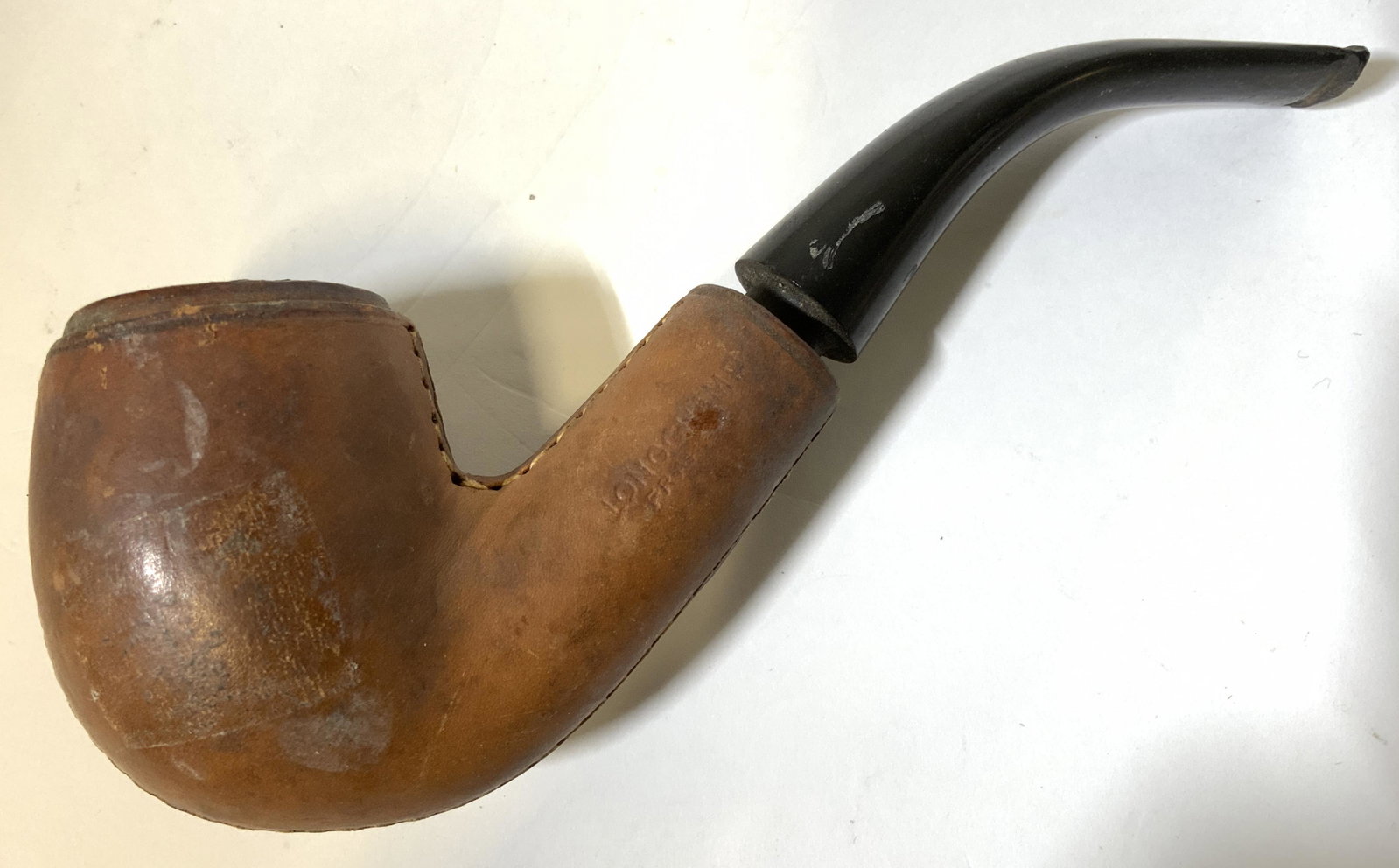 LONGCHAMP Antique Hand Stitched Leather Pipe: Piece is marked LONGCHAMP FRANCE Pipe is brown toned leather with hand stitching. Mouthpiece is black toned. Piece measures approx 5.5 inches long 3 inches tall, 1.5 inches wide. Pipe, LONGCHAMP, LONG