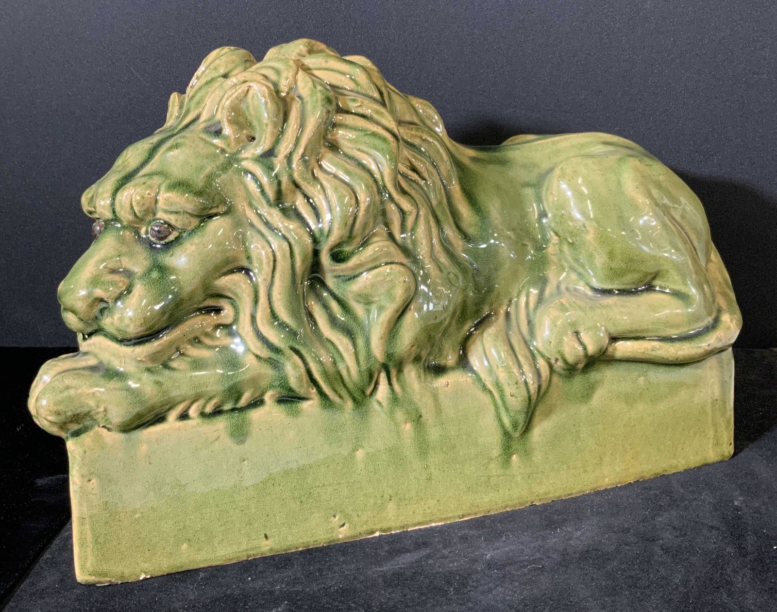 Vintage Green Glazed Ceramic Reclining Lion Statue: Vintage green glazed ceramic lion statue. Lion is pictured reclining. His head rests upon his front paws. Embossed ceramic mane and facial details. Underside of statue has felt pieces towards each cor