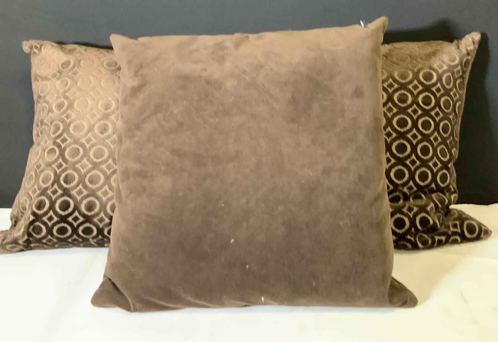 Set 3 Brown Velvet Throw Pillows: Three brown feather down throw pillows. Two pillows have circular deep brown designs, while the third is a solid chocolate brown. All three pillows have zippers. Interiors of all three have feather do