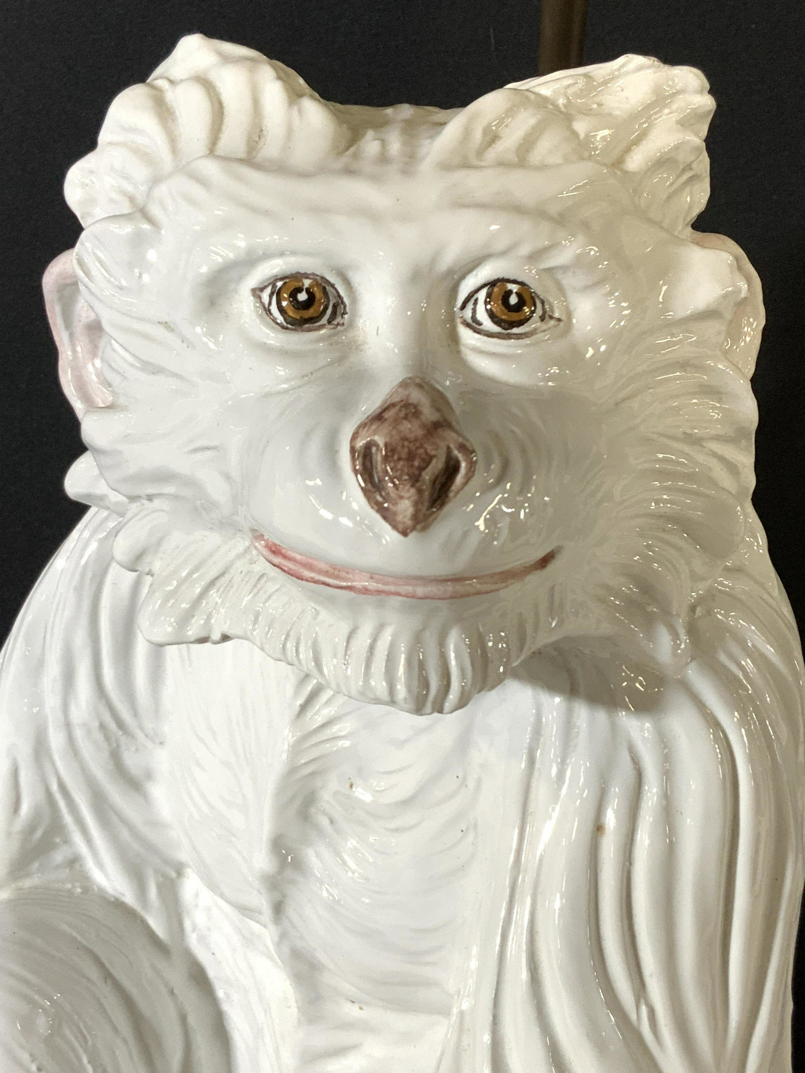 White Porcelain Monkey Statue Table Lamp: A white porcelain monkey with embossed porcelain hair accents throughout. The monkey has hand painted facial details, pink lips, hazel eyes, and a brown nose. The monkey is depicted smiling and seated