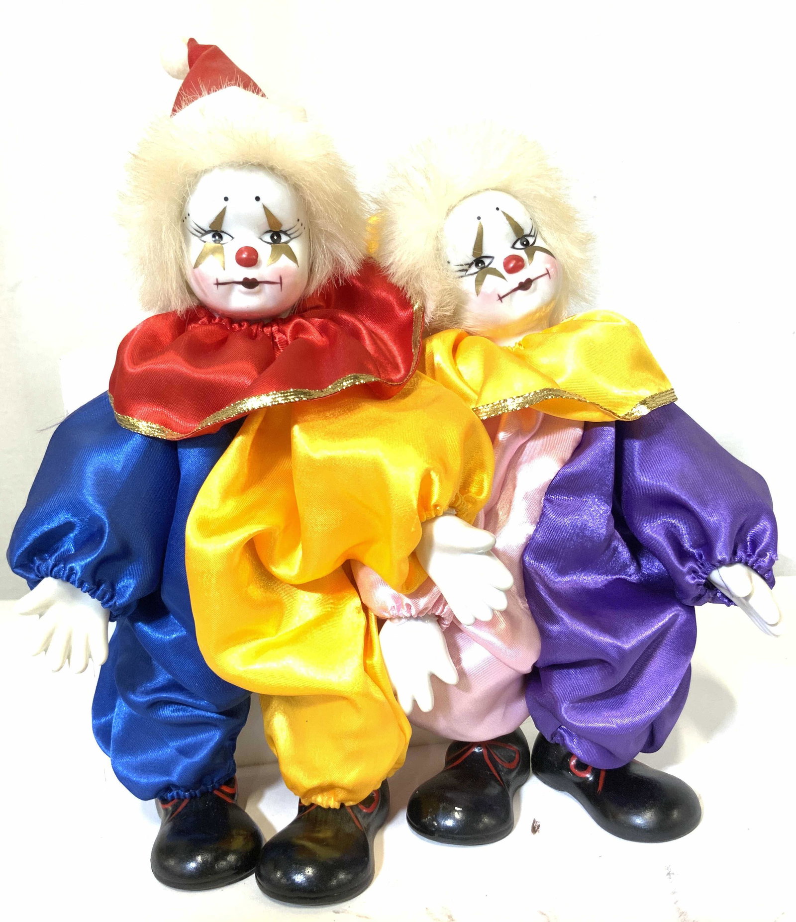 Pair Hand Painted Porcelain Circus Clown Dolls: White ware porcelain hands and faces. Faces painted with stars around eyes, red button nose, plump limps and eyelashes. Oversized painted black porcelain clown shoes. Clowns dressed in traditional cir