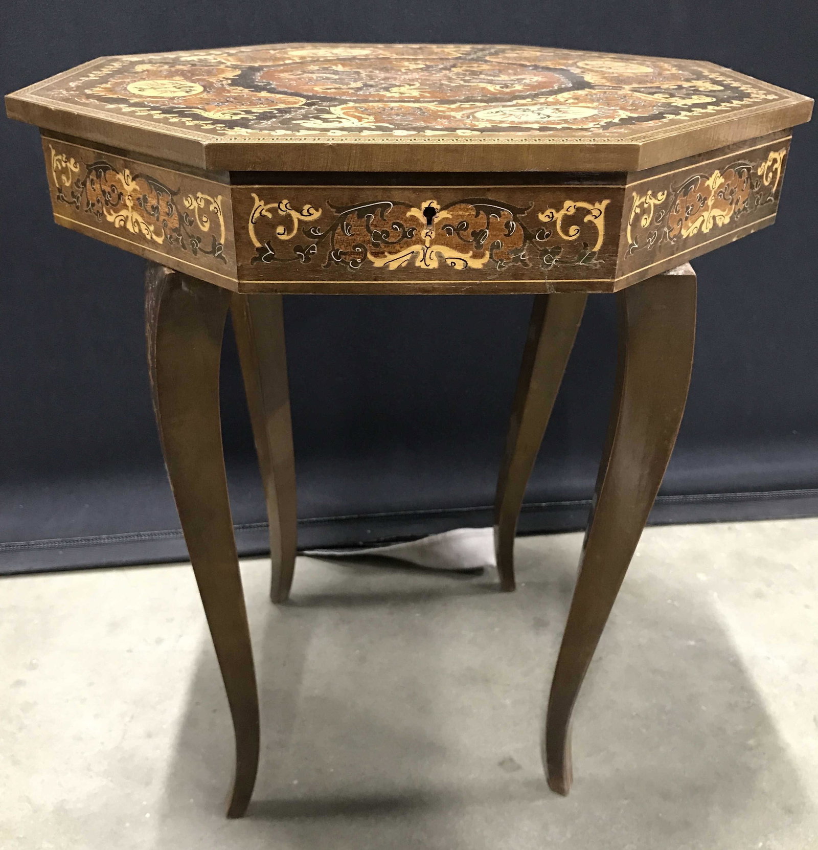 Vintage Music Box Side Table: Side table has octagon shaped top lid. Piece has tones of brown, beige & tan with intricate ornate detail piece has 4 slightly curved legs. Piece measures approximately 17.5 inches tall 15.5 inches wi