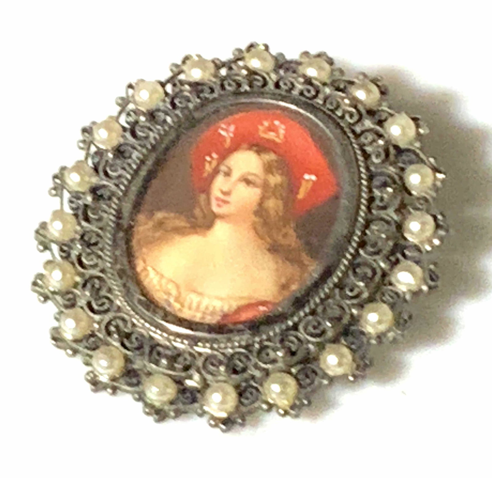 Silver Victorian Filigree Portrait Pendant: Pierced metal broach or necklace pendant (has bail & pin closure). Filigree backing is adorned with small pearls. Centered portrait of a woman in a red hat. Backing is silver, reads 800, which means 8