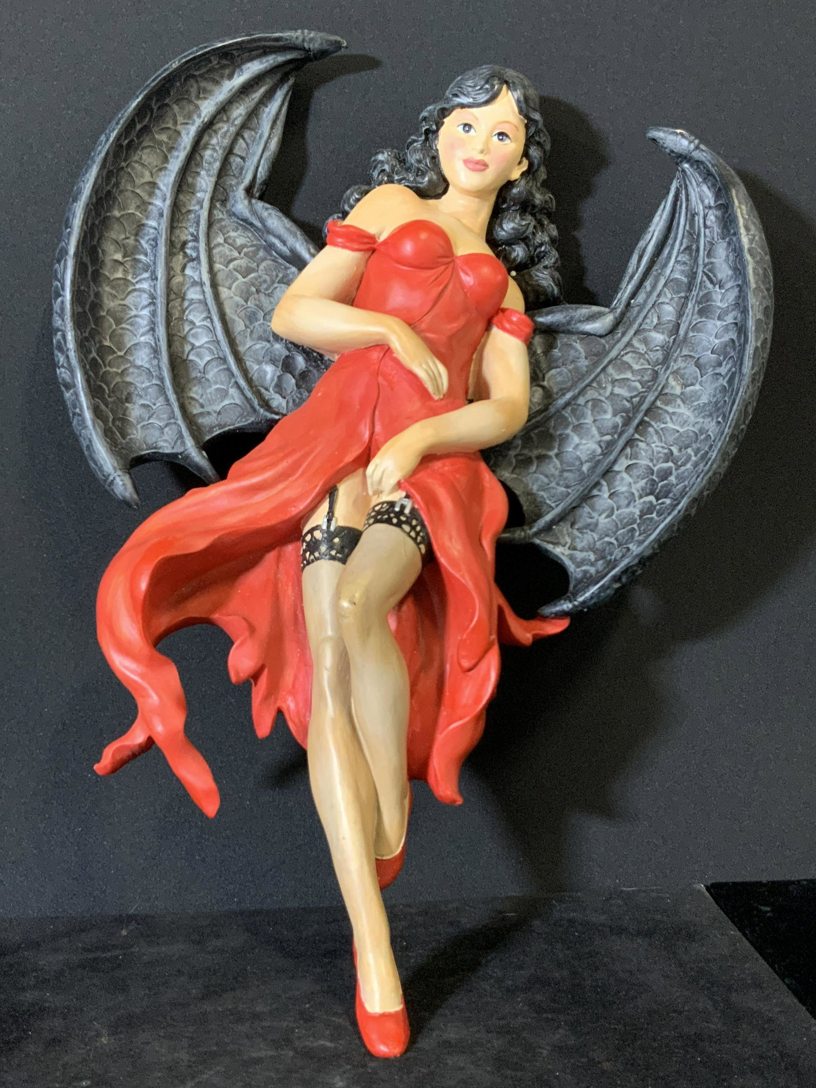 TOSCANO Woman In Red W. Black Wings Sculpture: This composite sculpture depicts a woman in a red dress and garters with black wings. Etched details in the material add depth to the piece. In relief accents on wing veins and facial features. The un