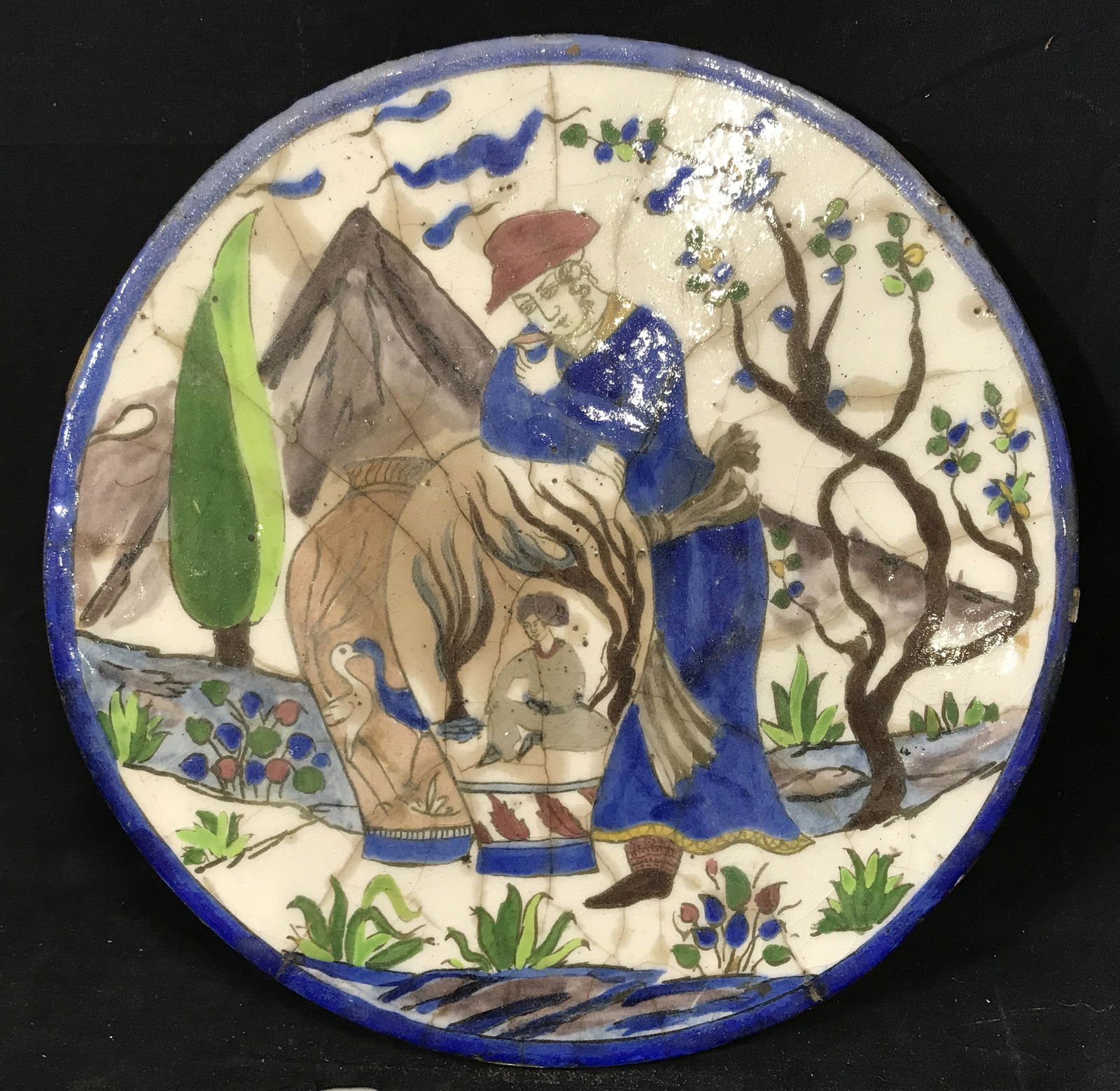Antique Persian Tile Artwork: Antique Persian tile, piece displays a man in blue robes drinking from a small cup while leaning on two large pots, cracks to tile, blue border painted along the edge, measures 15.75 inches at tallest