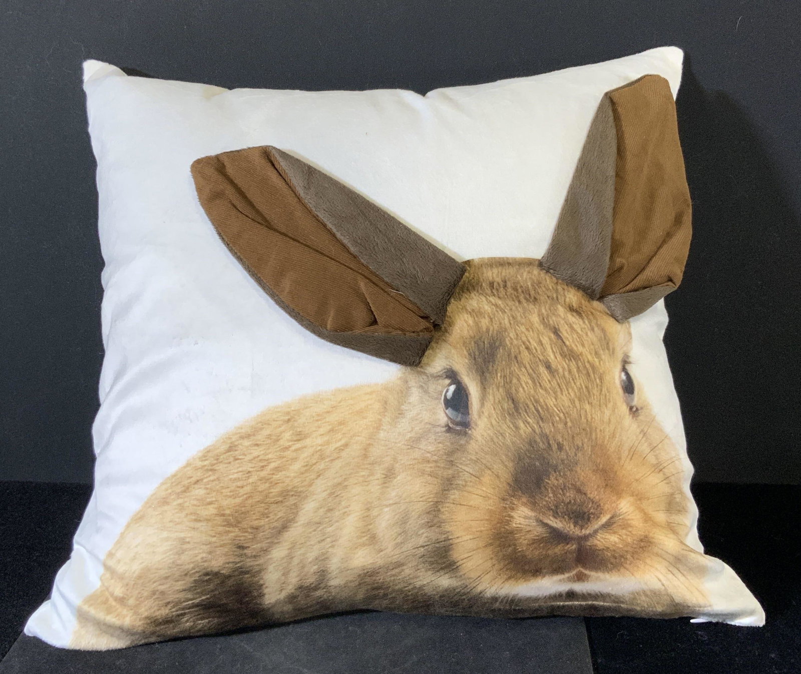 Polyester Rabbit Portrait Throw Pillow: A white polyester pillow with a brown rabbit portrait on the front side. The rabbit’s ears are in relief of the pillow surface. Soft hand fabric. One white zipper. Interior pillow insert is 100% pol
