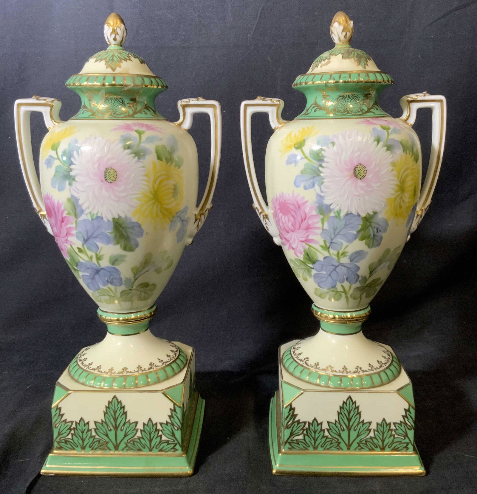 Pair NORITAKE Hand Painted China Urns: Pair NORITAKE China Urns, stamp to base reads ‘NORITAKE Handpainted Japan’, intricate painted floral and vegetal design, both measure 13 inches tall x 4 1/4 inches wide at base, one lids handle ha