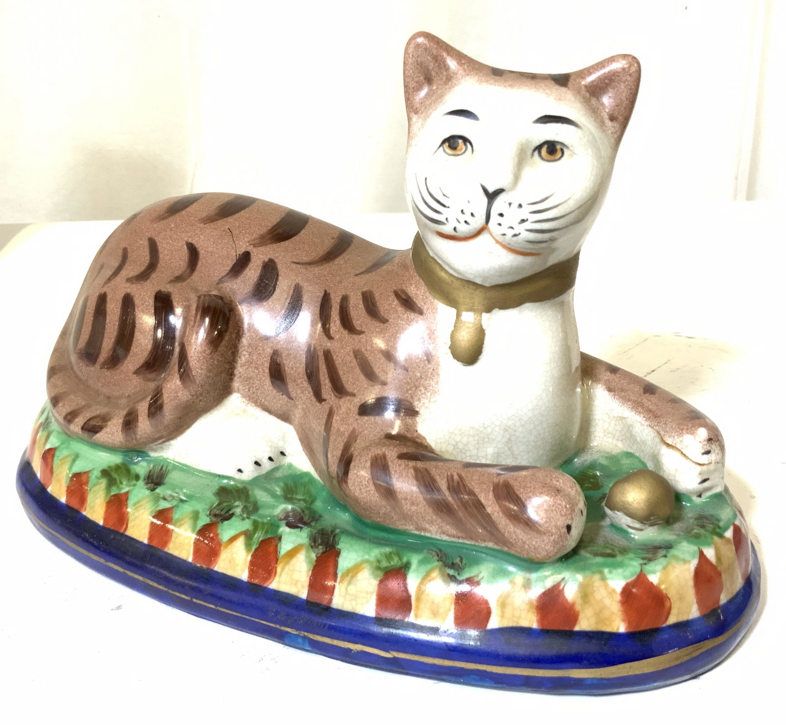 Pair ANTIQUE STAFFORDSHIRE Porcelain Cat Figurals: Ceramic Cat Statues, hand painted ceramic cats with bell collars. Cats have a toy ball between paws. Faces are very human like, a ‘ Cheshire smirk’ . Surface glaze crazing consistent with age. 10 