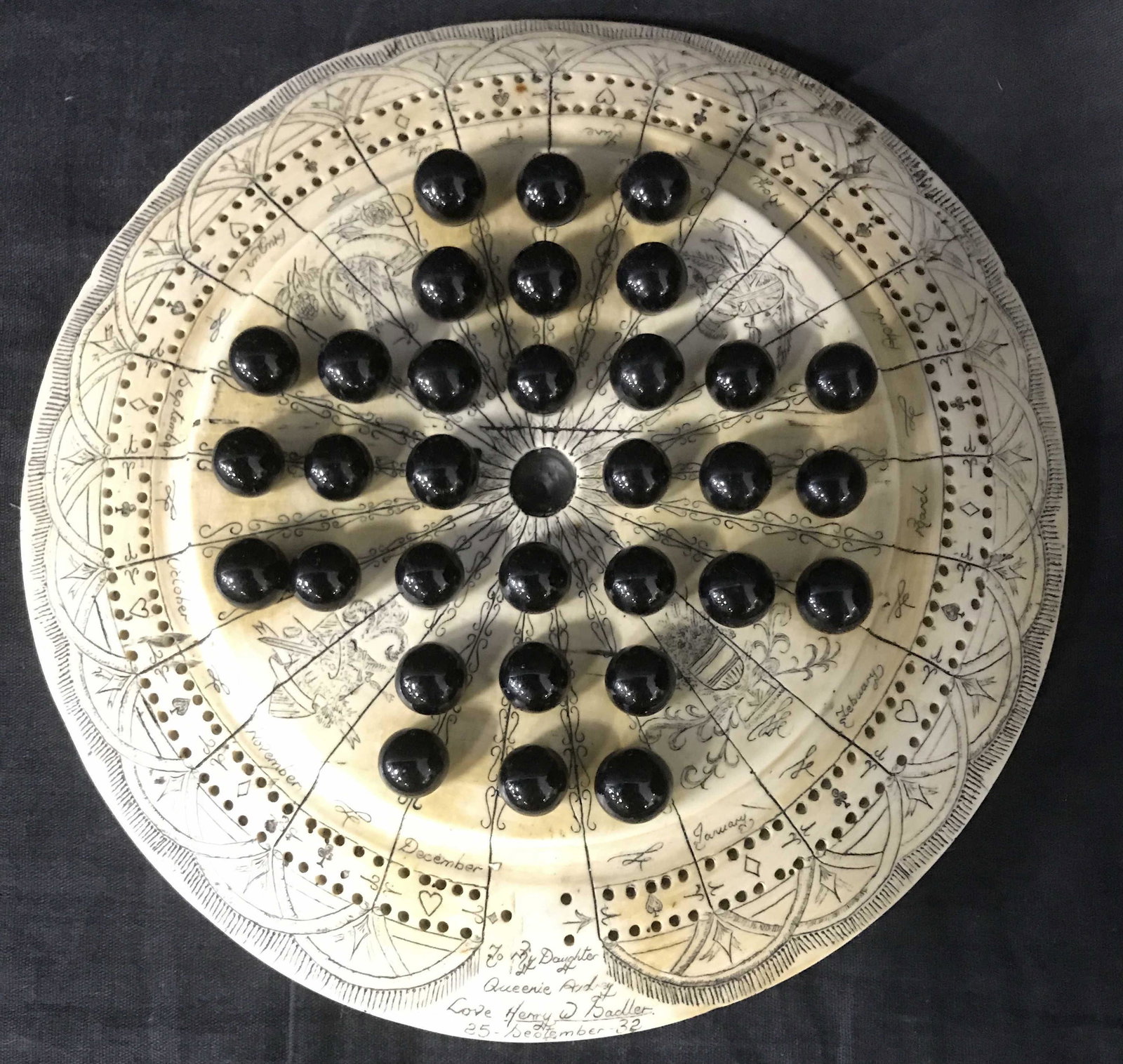 Vintage Peg Solitaire Scrimshaw Board w Marbles: Vintage, possibly antique, peg solitaire board. Board appears to be bone, possibly faux. Detailing is intricate, inscriptions list the months, card suit icons, and various other detailing. Measures ap