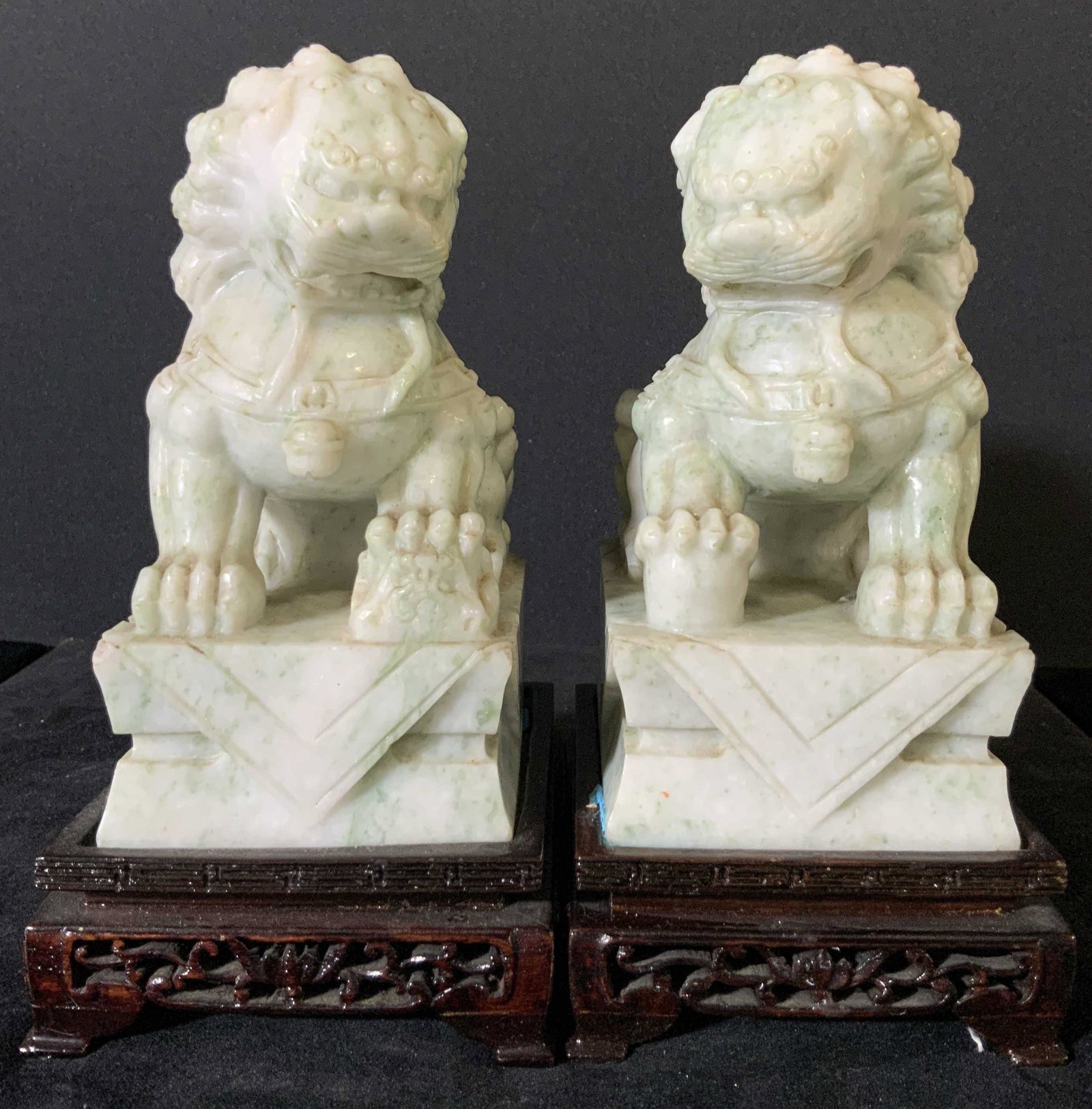 Pair Carved Chinese JADE Fu Dogs W. Wooden Stands: A pair of Asian Foo Dogs / Fu Dogs carved from mottled jade. The jade is light in color overall, with splashes of a deeper green jade color throughout. Both fu dogs are finely incised with muscular bo