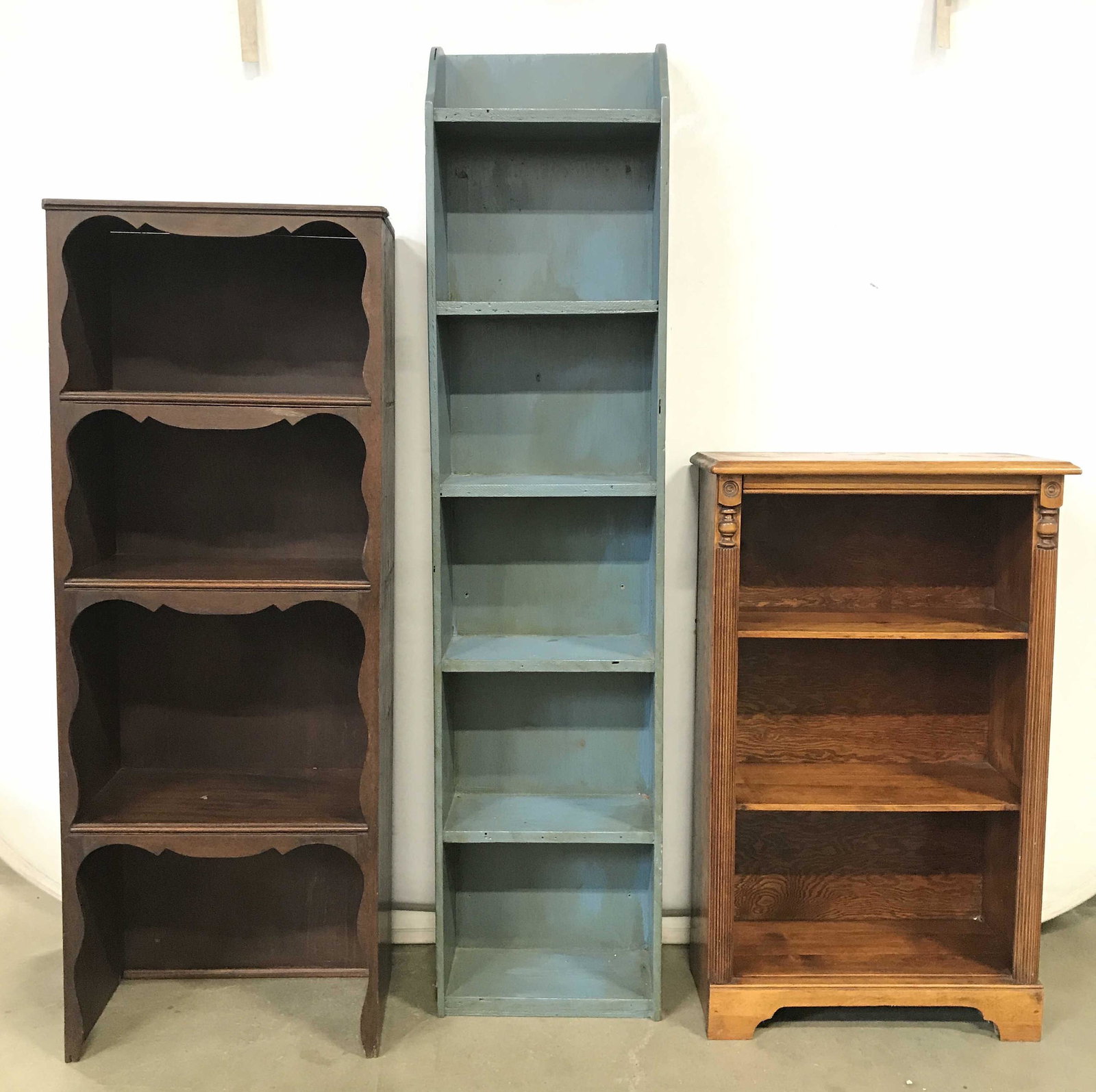 Lot 3 Antique Wooden Bookshelves: Lot includes 3 wooden bookshelves. One is blue toned, hand painted with country style, primitive style. Blue toned shelf has 4 shelves, brown toned shelf has 3, beige toned shelf has 2. Tallest piece 