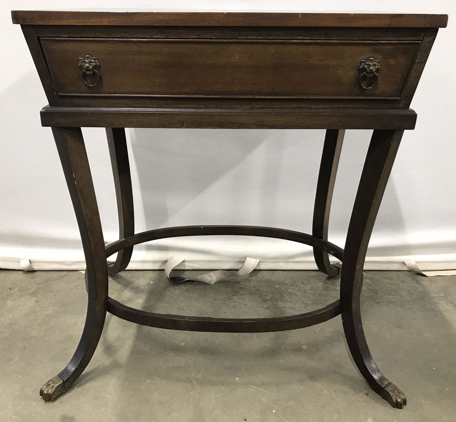 Vintage Carved Wooden Side Table W Paw Feet: Side table is vintage and wooden. Piece is brown toned. Side table has 1 drawer on long side. Piece also has 4 curved wooden legs with gold toned brass feet. Table has oval shaped stretcher in between