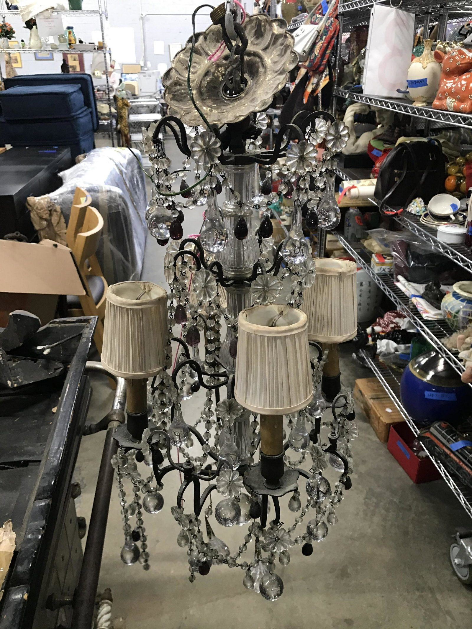 Vintage 4 Arm Metal Chandelier W Shades, Prisms: Chandelier is vintage possibly antique. Piece has an assortment of variously shaped ornaments. Piece has 4 arms each with candlestick style bulb sockets & shades. Chandelier Measures approximately 23 