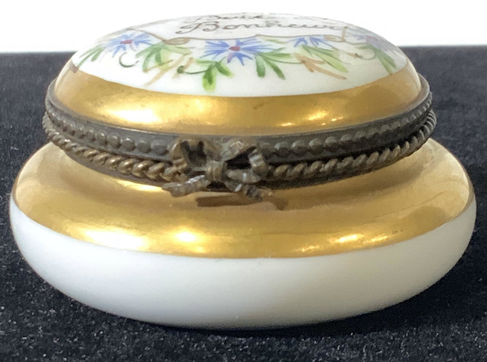 FRENCH SEVRES ‘Happiness’ Porcelain Pill Box: Hallmarked porcelain box, mark on verso in blue ink directly on porcelain. Possibly Sevres. Mark unidentifiable. Hand painted long with bright blue and green florals. Gilt borders flank bronze articul