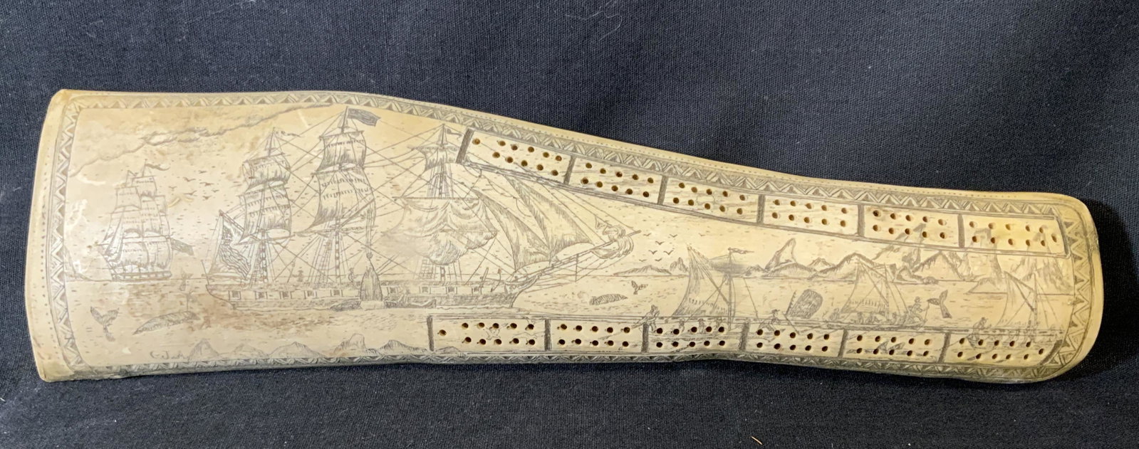Signed Faux Scrimshaw Cribbage Board: Faux scrimshaw, features etchings of detailed ships, riggings, masts, whales, seas, and clouds. Cribbage board drilled into piece. Outer edge has geometric etched banding. Illustration is signed in lo
