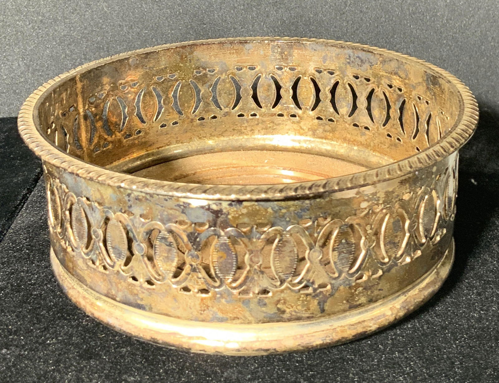 Vintage Open Metalwork Tabletop Wine coaster: A vintage, possibly antique, metal wine coaster dish with a polished antiqued silver coloring. The interior of this dish is wooden with carved circle accents. The underside possesses green felt. The o