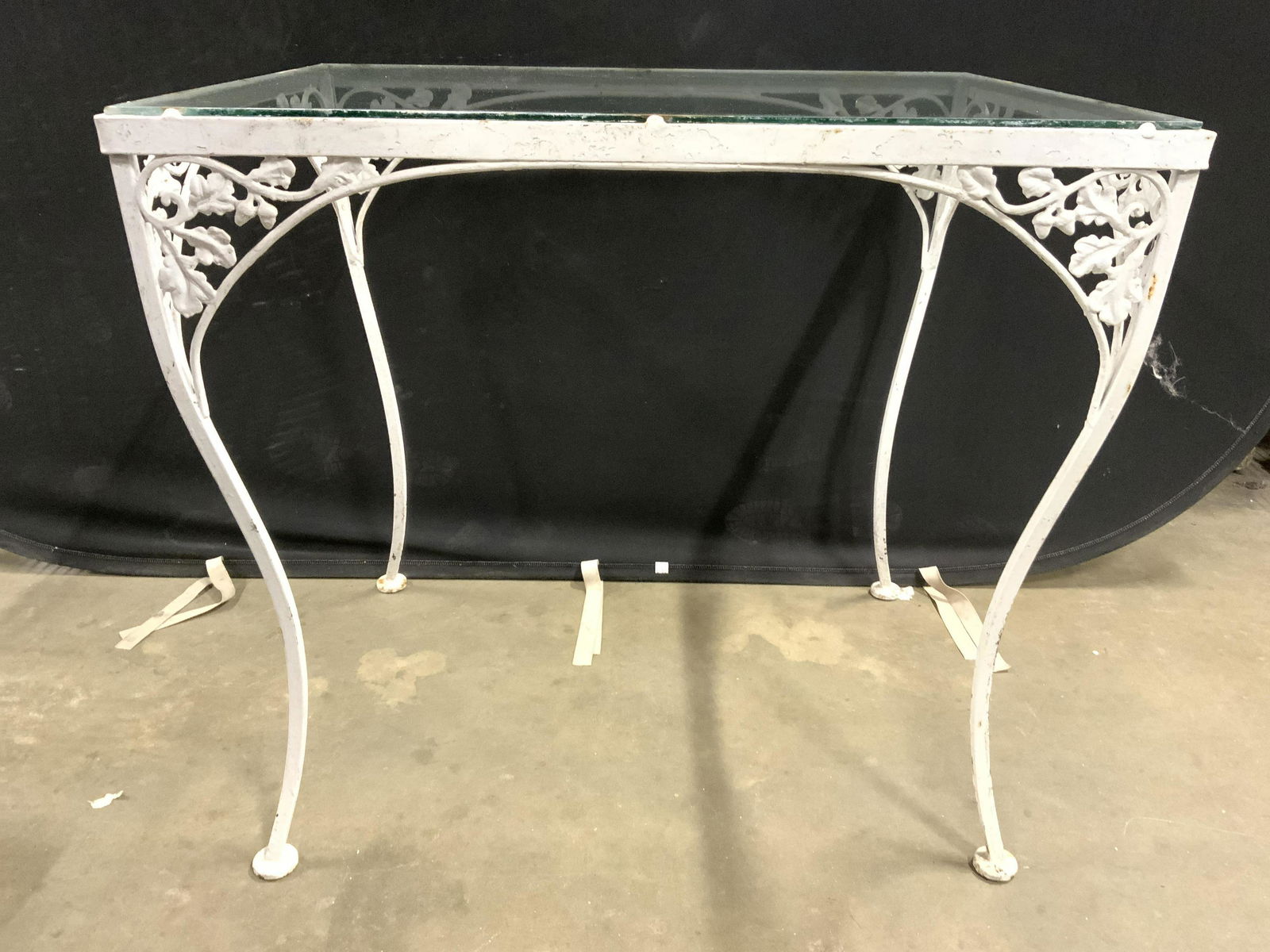 Vintage Outdoor Metal Glass Top Table: Table is vintage possibly antique. Base is white toned and metal with leaf & vine detail. Table has 4 legs each with circular feet. Tabletop is glass. Piece measures approx 30 inches tall 33 inches wi