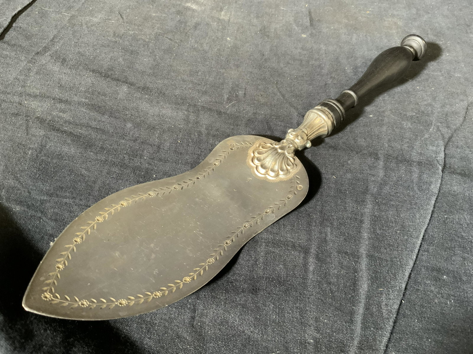 Silver tnd Serving Cake Knife Sercer: Silver tnd serving knife, no apparent inscriptions or labels, subject a serving knife with vine like designs to the rim, black wooden handle, piece measures 12 inches in length and weighs 125 grams, o