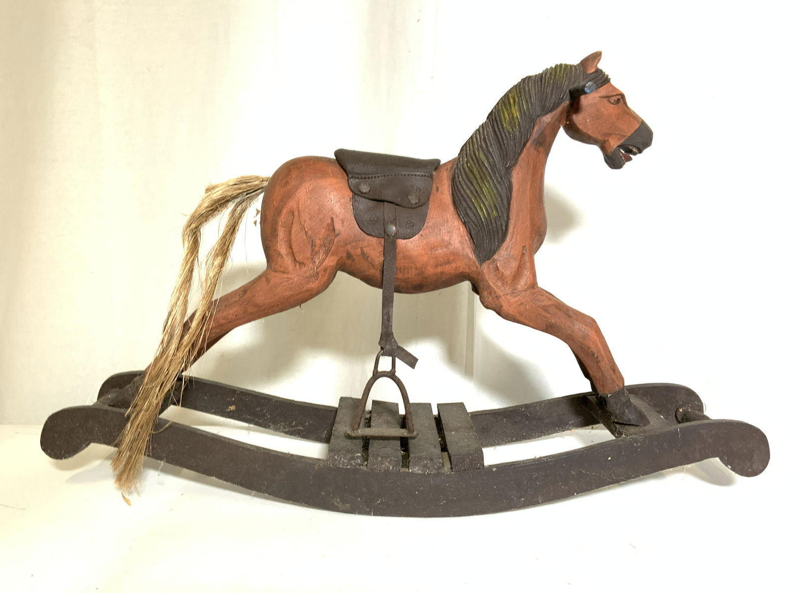 Antique Folk Art Rocking Horse: Antique, wooden, folk art rocking horse. Piece is hand painted, and handmade. Saddle is crafted from leather, the stirrups are iron, the horse and base are carved wood, the tale is crafted from straw.