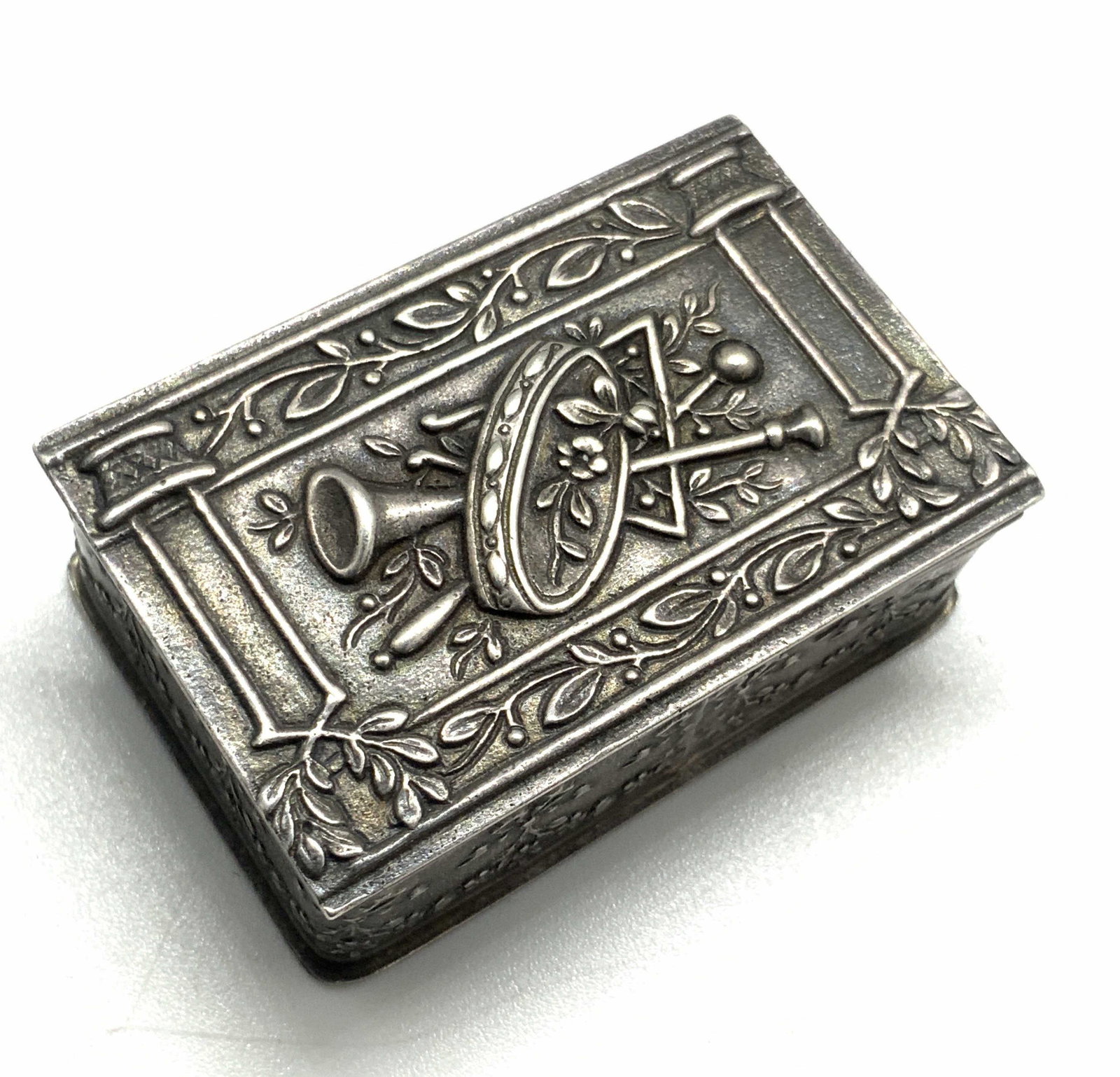 Vintage French Hallmark Sterling Silver Pill Case: Vintage French sterling silver pill case. The piece has etched and embossed designs along the lid and all sides. The design on the lid depicts a trumpet alongside a tambourine and flowers. The designs