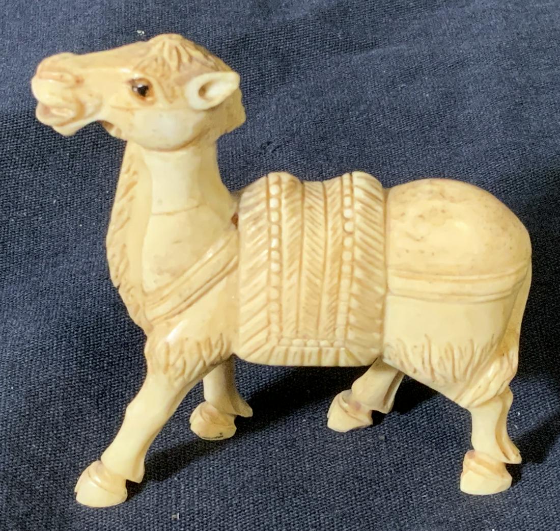 Hand Carved Bone Camel Figural: Hand carved bone camel statue, no apparent inscriptions or markings, subject a camel mid step with a saddle on its back, piece measures 3 inches at tallest point, piece is missing an ear, eyes are pai