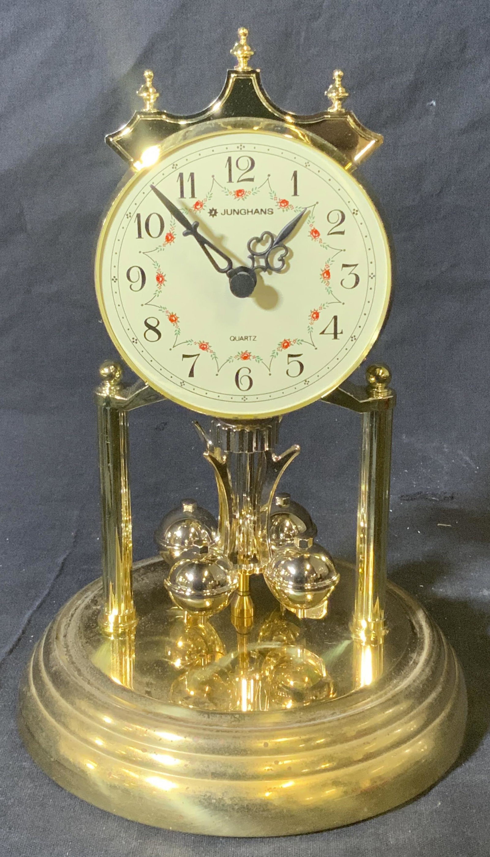 JUNGHANS Quartz German Desk Clock: Junghans Quartz German Clock, face of clock reads ‘Junghans’ and ‘Quartz’, face of clock display plain numbers and rose floral designs, piece is made of a gold toned composite material, clock 