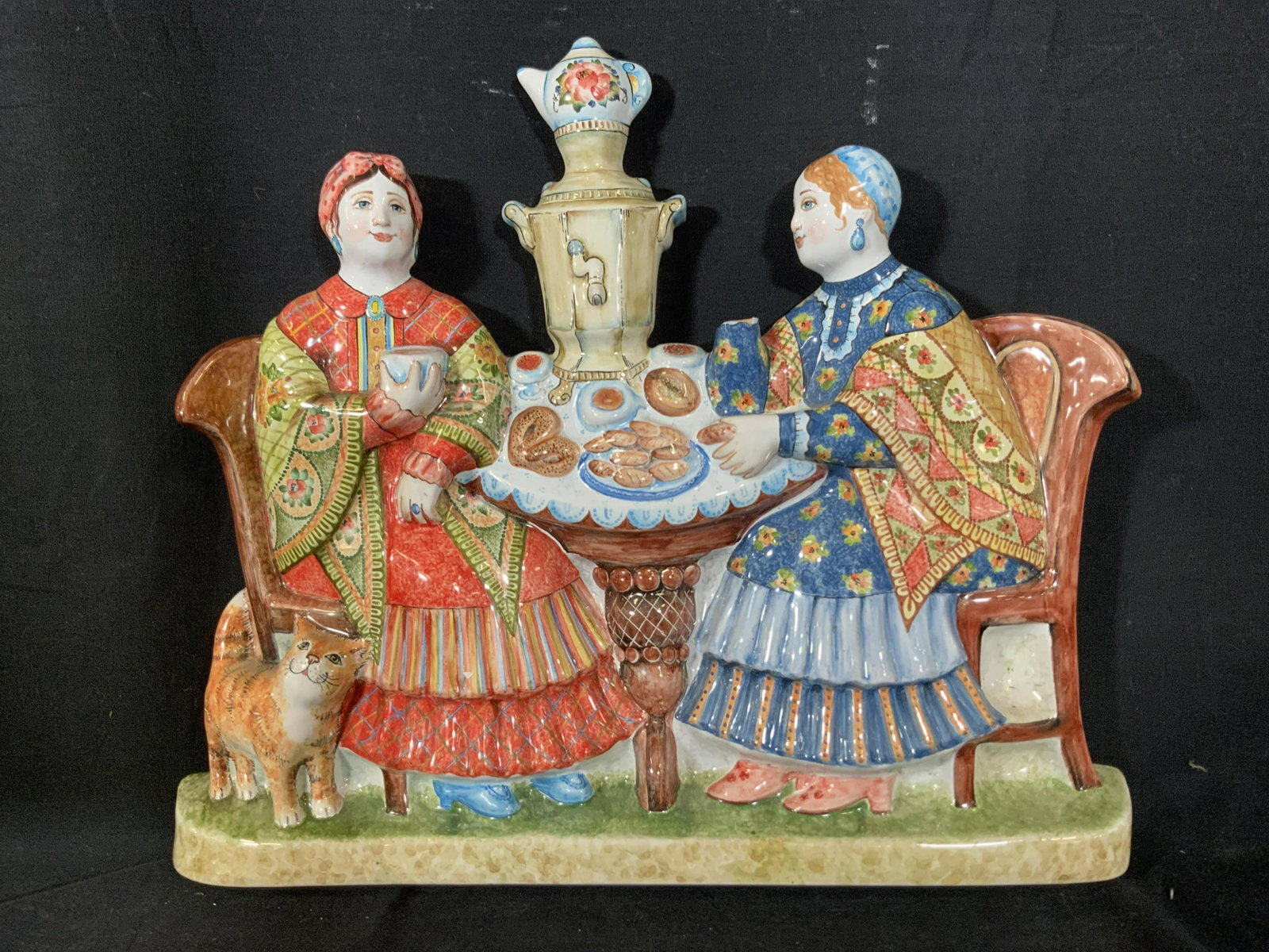 Hand Painted Russian Ceramic Wall Plaque: Ceramic painted glazed Russian Decorative wall art, plaque Scene of two women in fanciful attire seated at table with pastries and samovar, one holds ever, the other holds a mug, cat stands by chair, 
