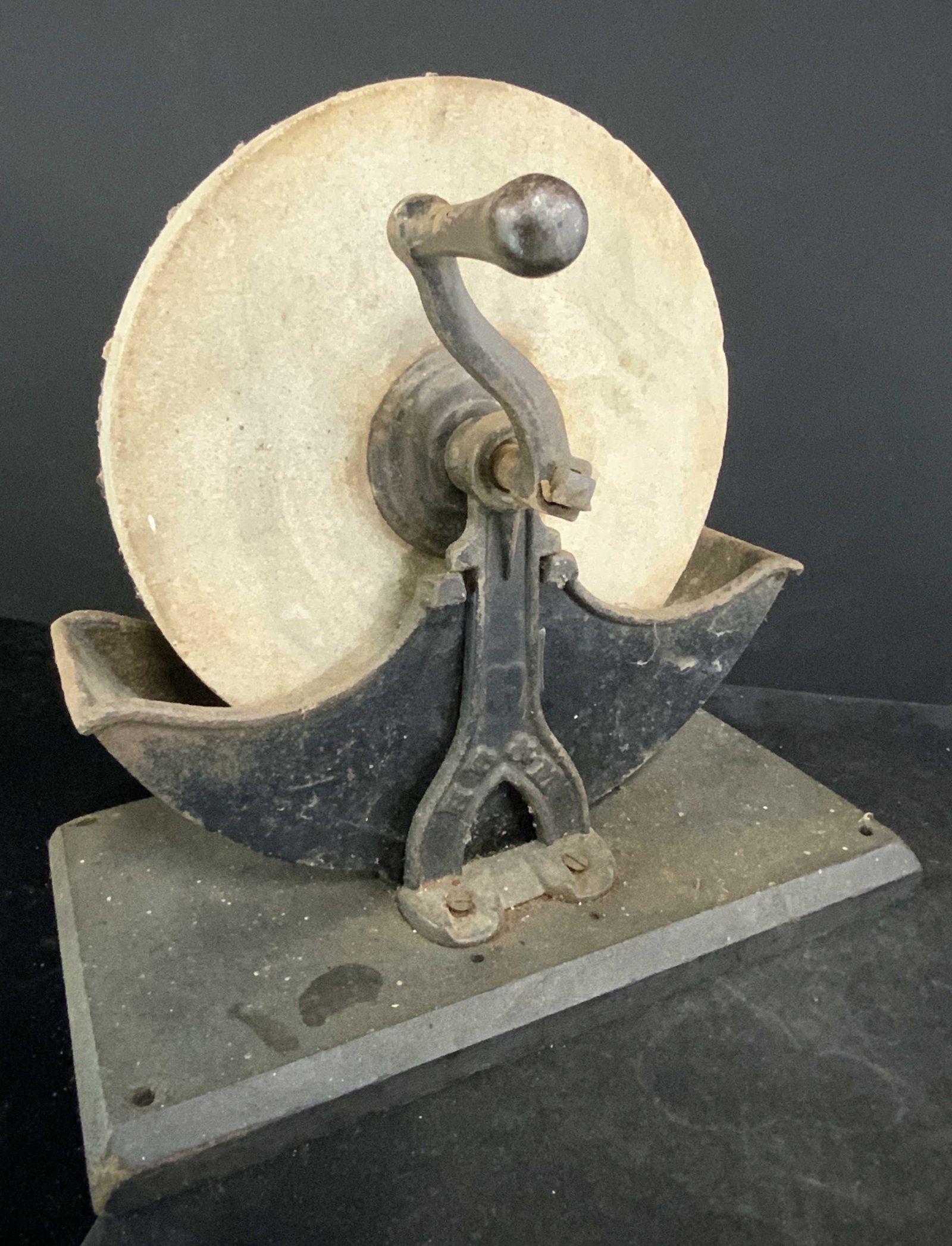 HB & M Signed Antique Iron & Stone Sharpening Tool: An antique stone sharpening wheel that operated via turning a hand crank. The base and hardware are crafted from iron. The wheel is crafted from stone. The hand crank still rotates the wheel. Once a t